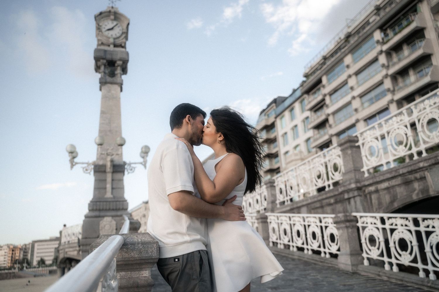 A romantic couple embraces on a classic European balcony with ornate architectural details and columns.