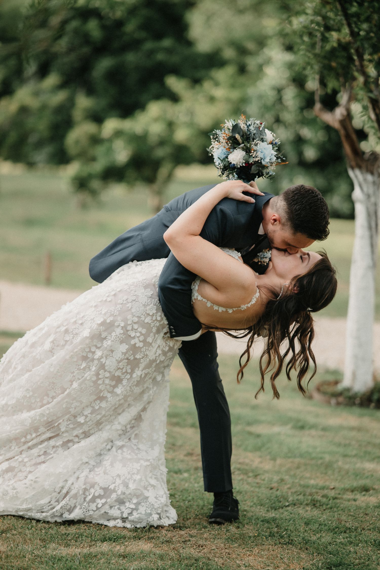 A romantic dip kiss sequence captured outdoors on a grassy lawn with trees in the background.