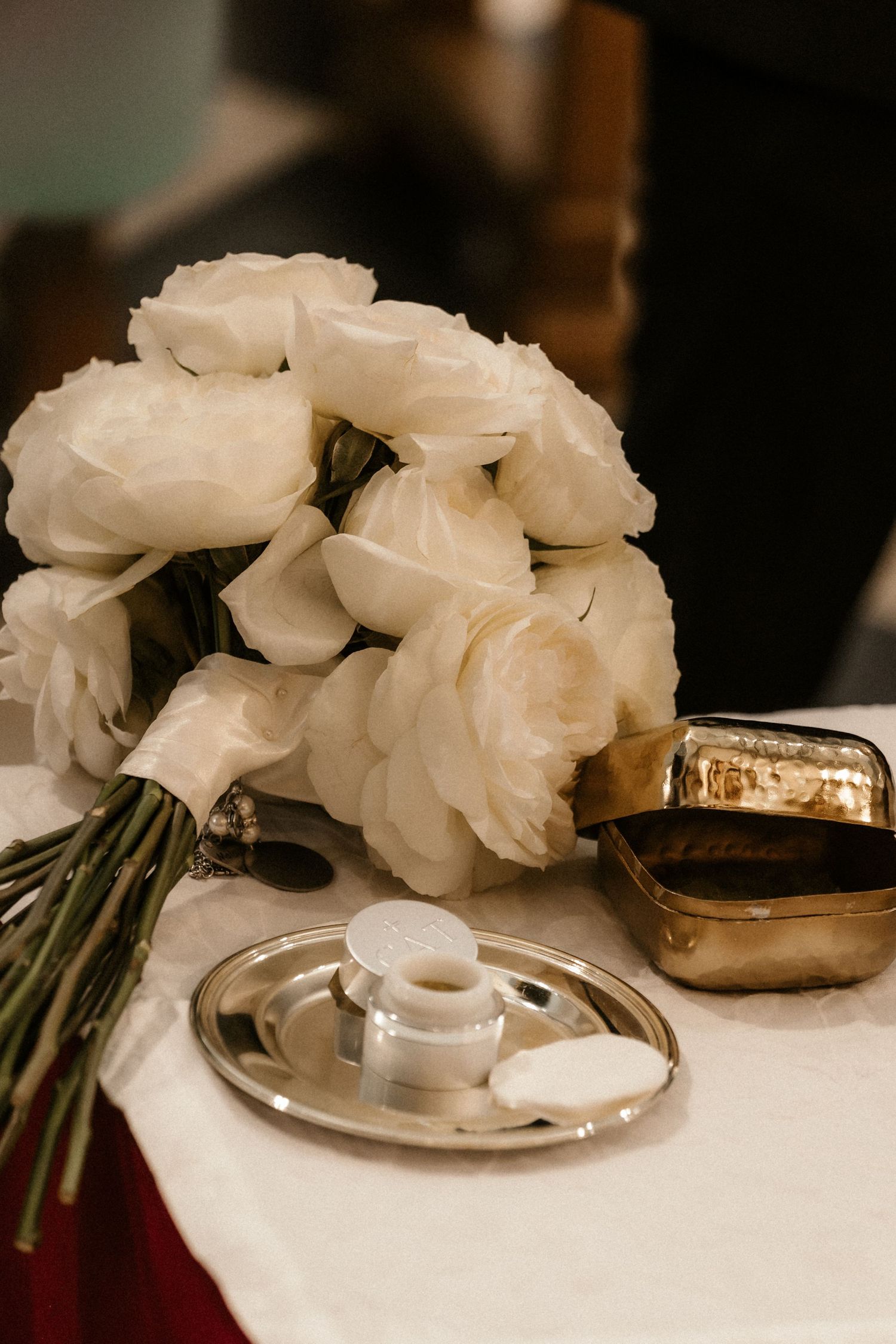 White carnation flowers rest beside gold wedding bands on a light colored surface in an elegant wedding detail shot.