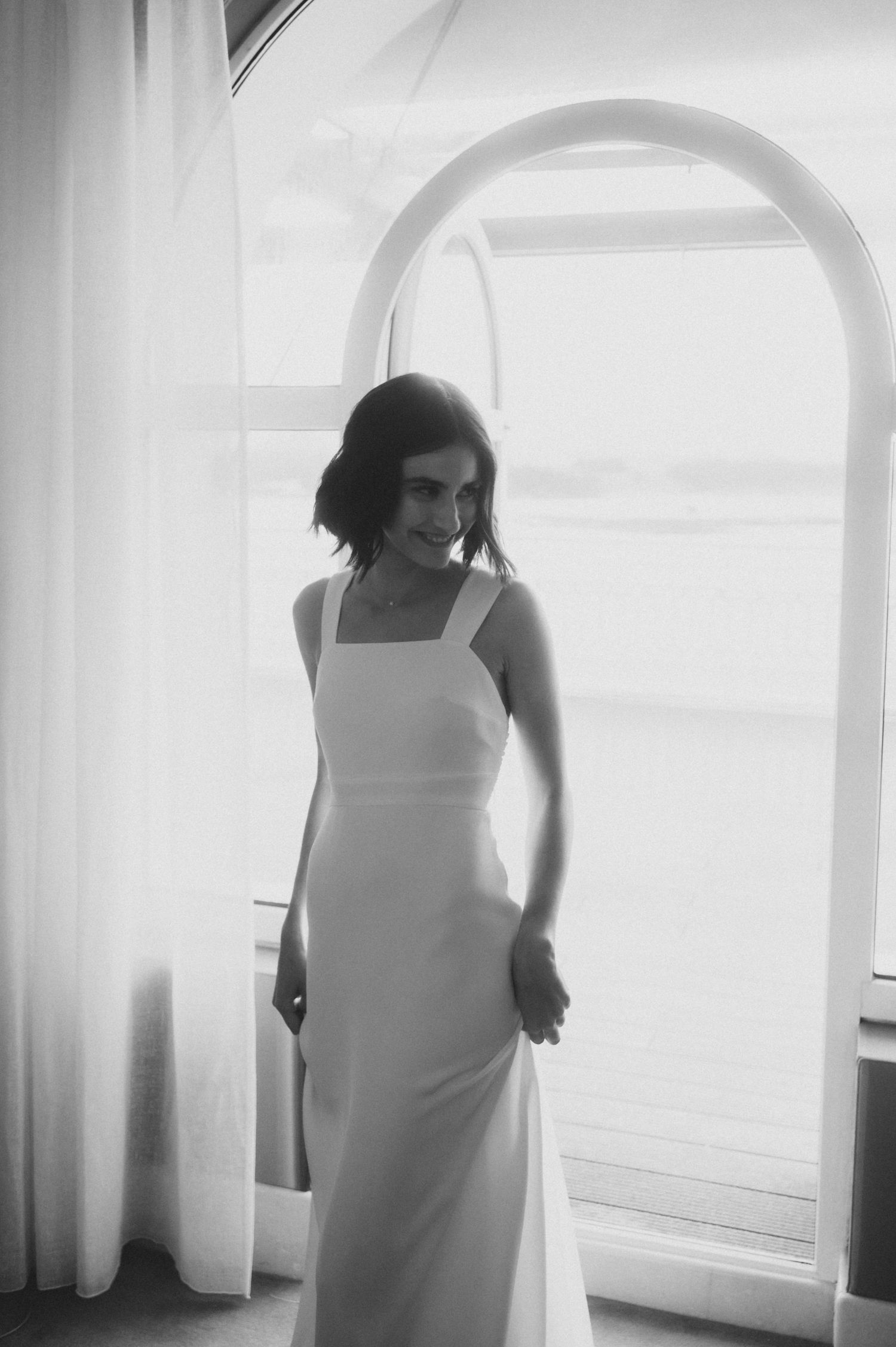 Artistic black and white photos capturing ethereal moments of a person in white dress by arched windows.