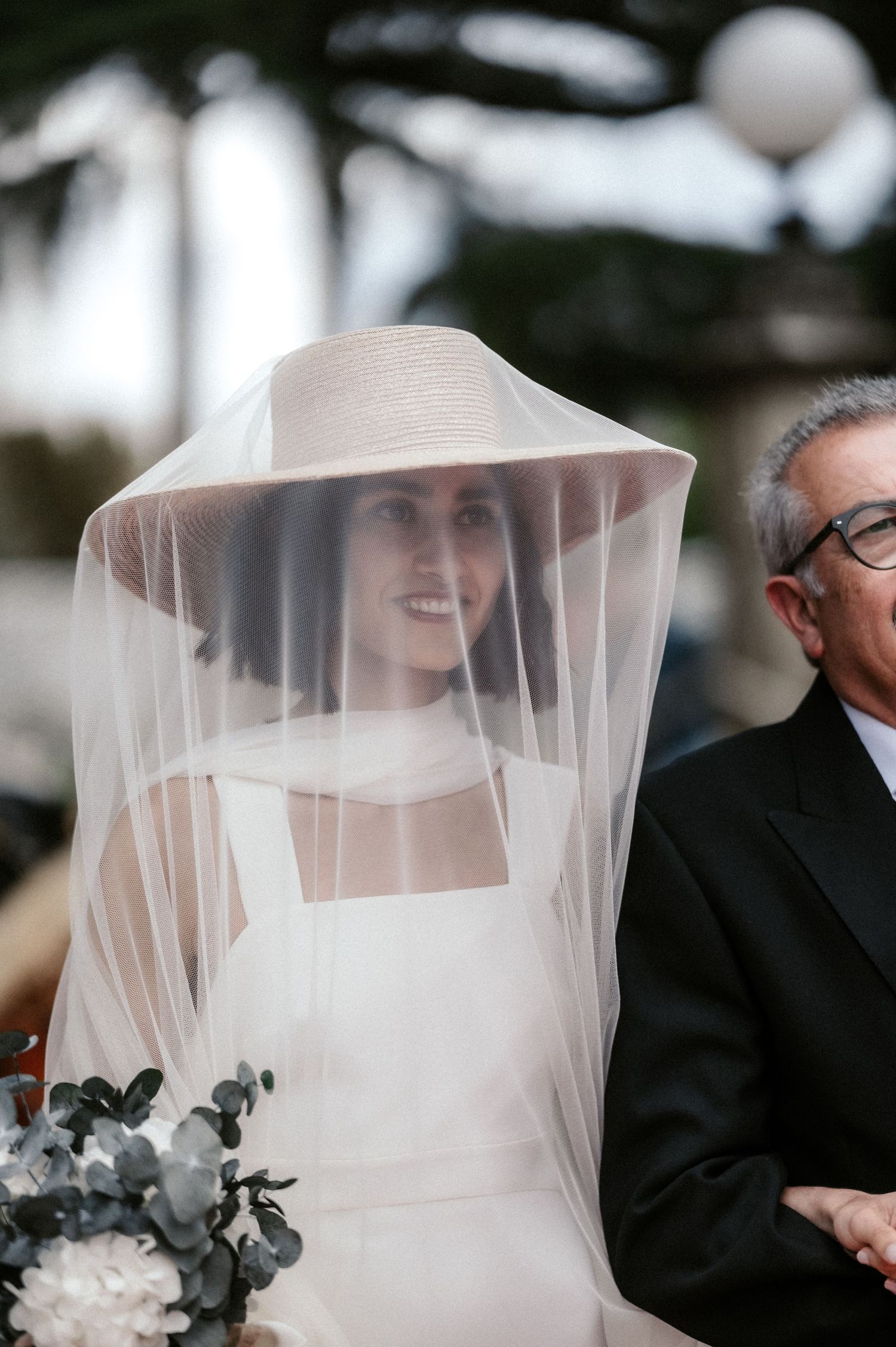 A bride wearing a delicate veil is shown in an artistic black and white wedding photograph.