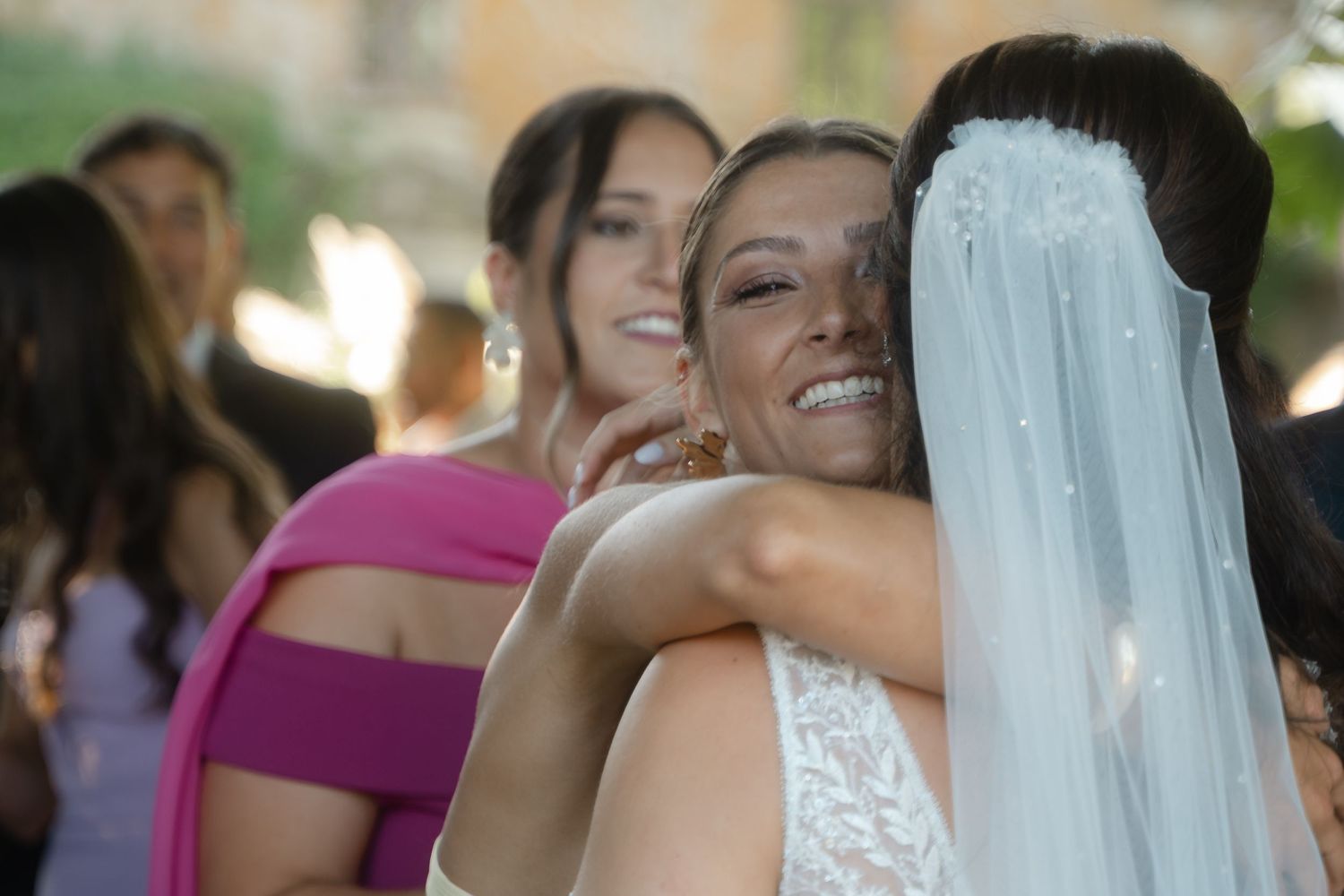 Wedding guests gather for emotional hugs and congratulations in a sunlit garden setting.