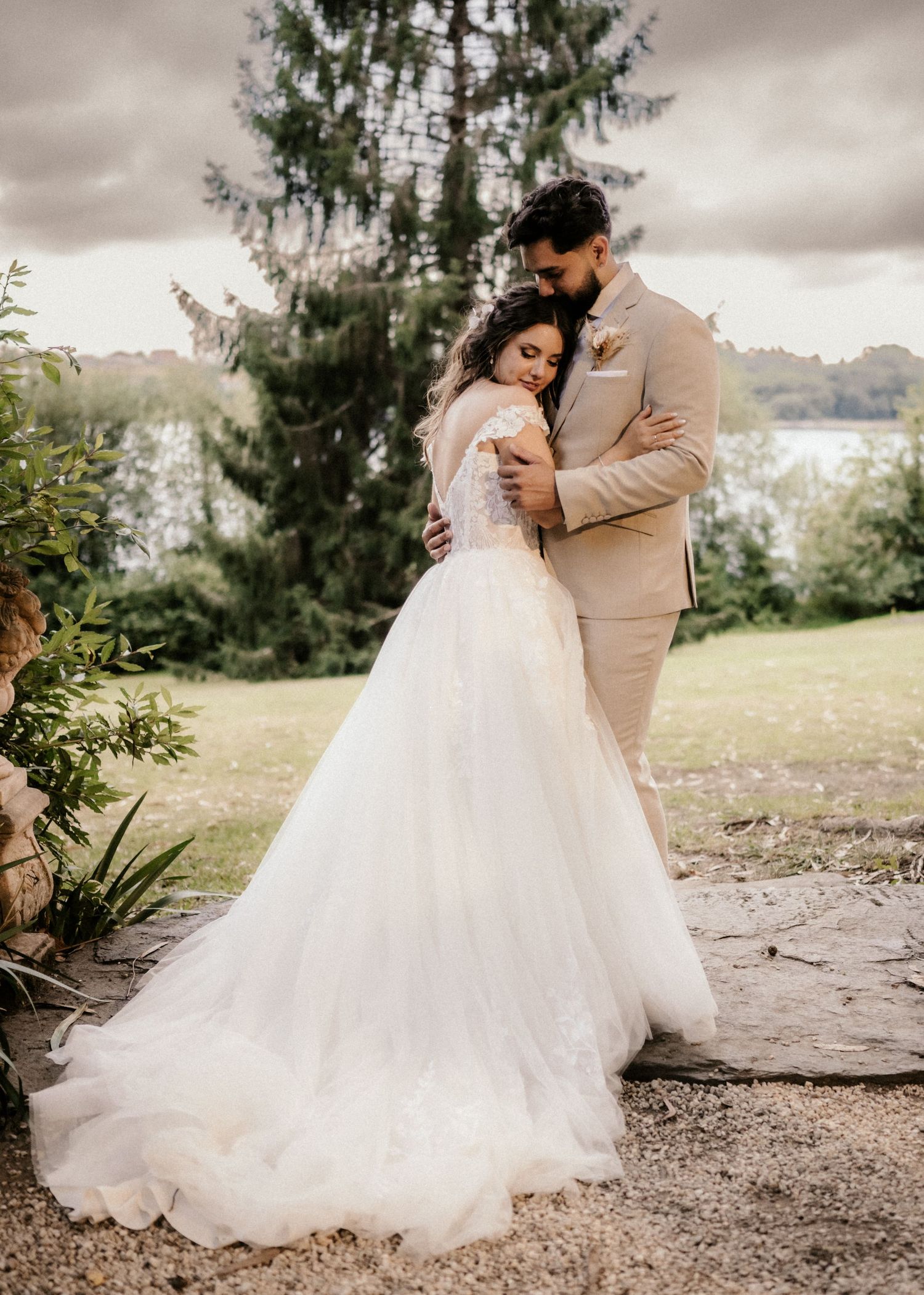 A couple in wedding attire share an intimate dance outdoors with a cloudy sky and trees in the background.