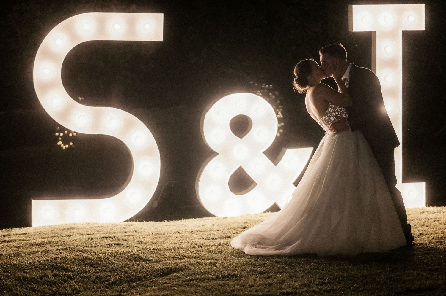Illuminated marquee letters create romantic lighting for a wedding photo at night.
