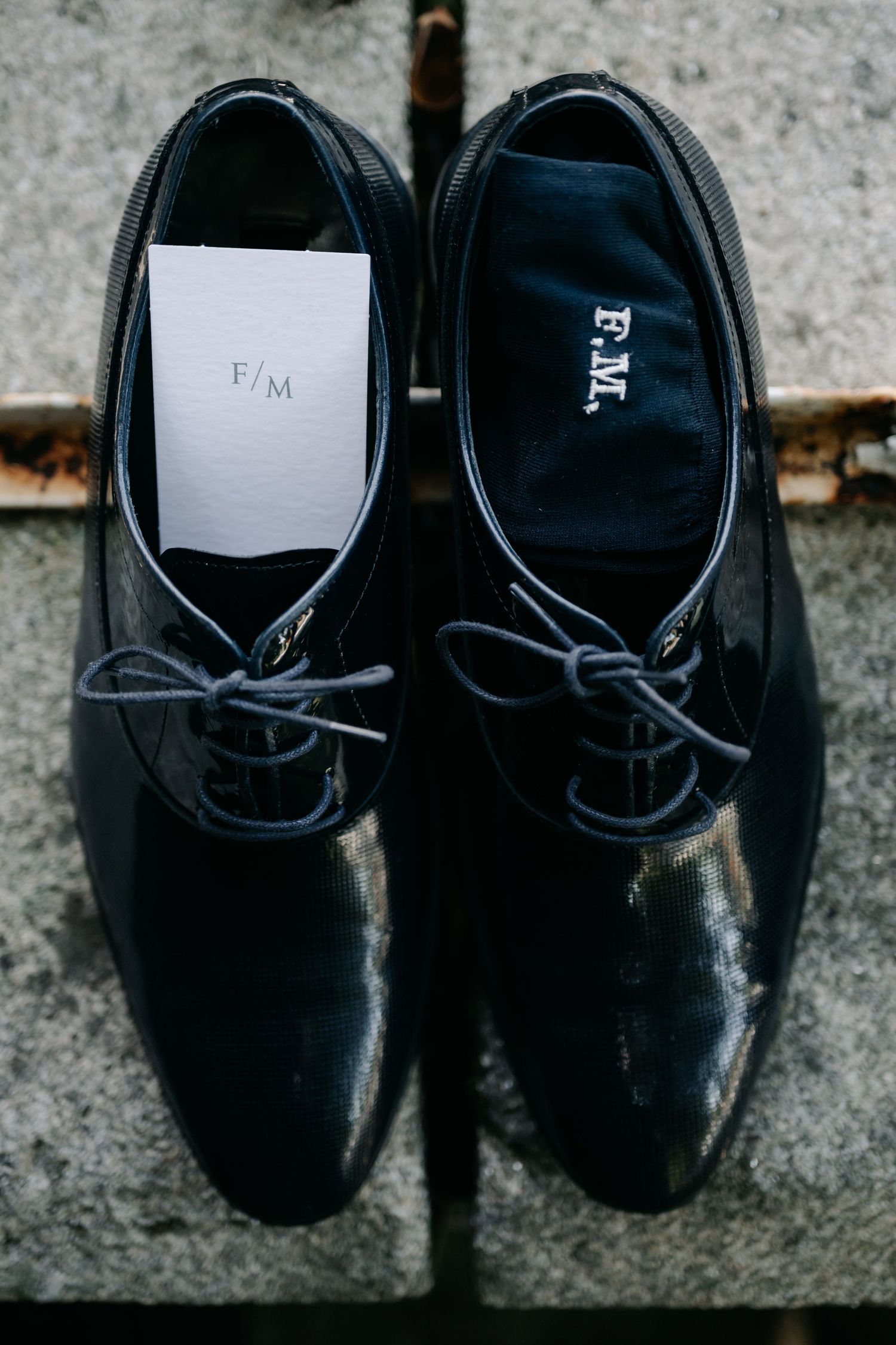 A pair of black leather dress shoes with gray laces sits on a concrete surface in a moody lighting setup.