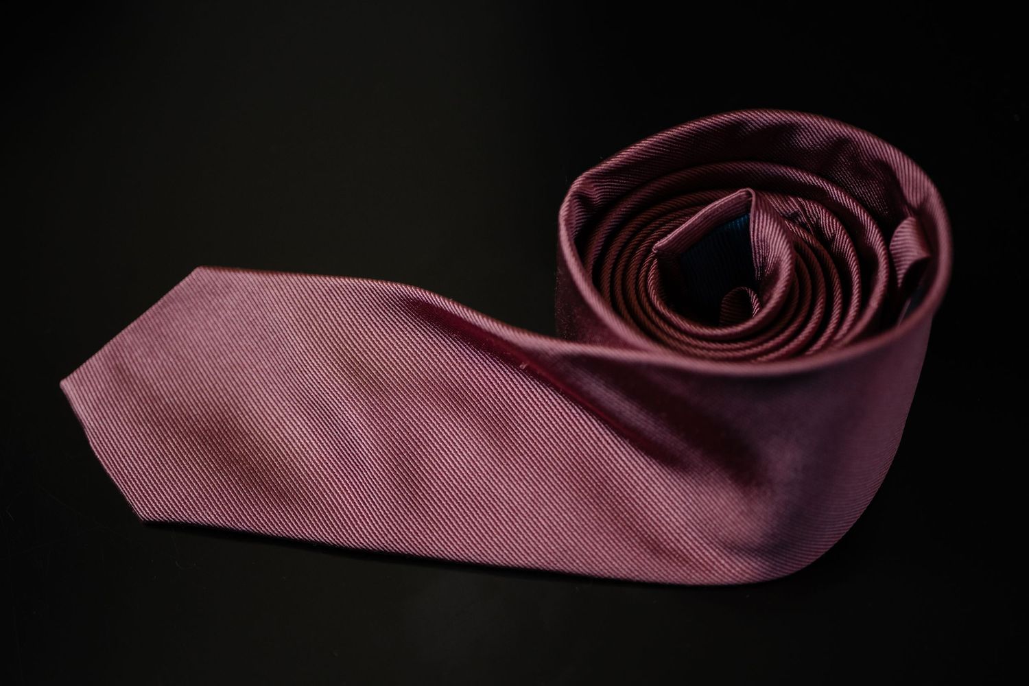 A sleek burgundy silk necktie elegantly coiled on a black background.