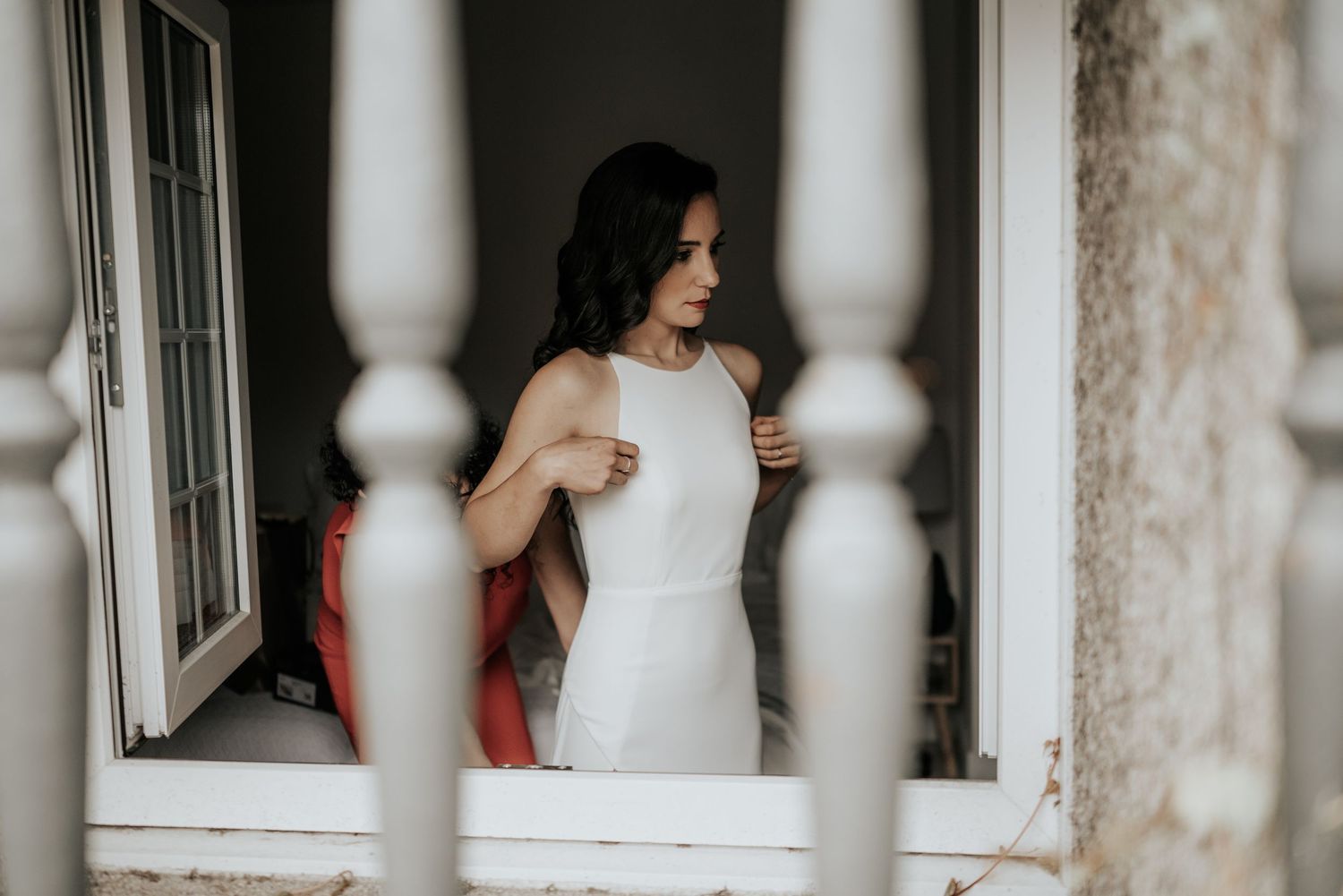 A couple sits together by a window with white railings in an intimate romantic moment.