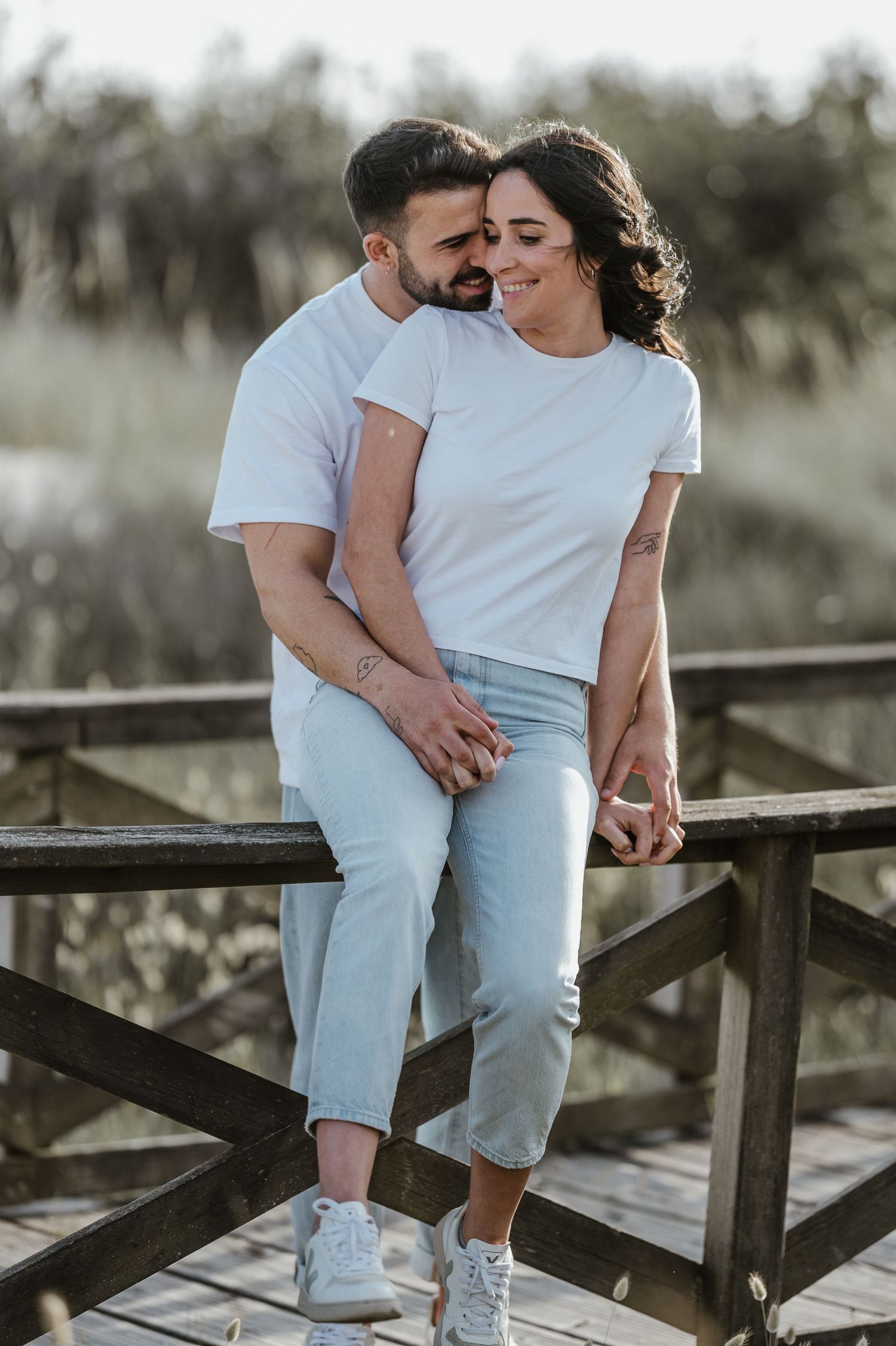 Romantic couple in white shirts and light denim sharing intimate moments on a wooden boardwalk or deck.