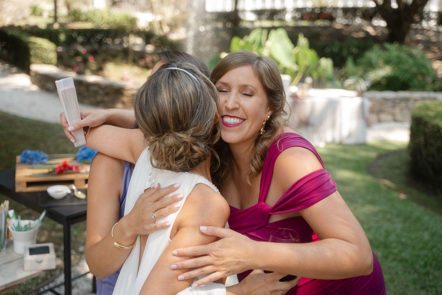 A group of people share joyful embraces and laughter during an outdoor celebration.