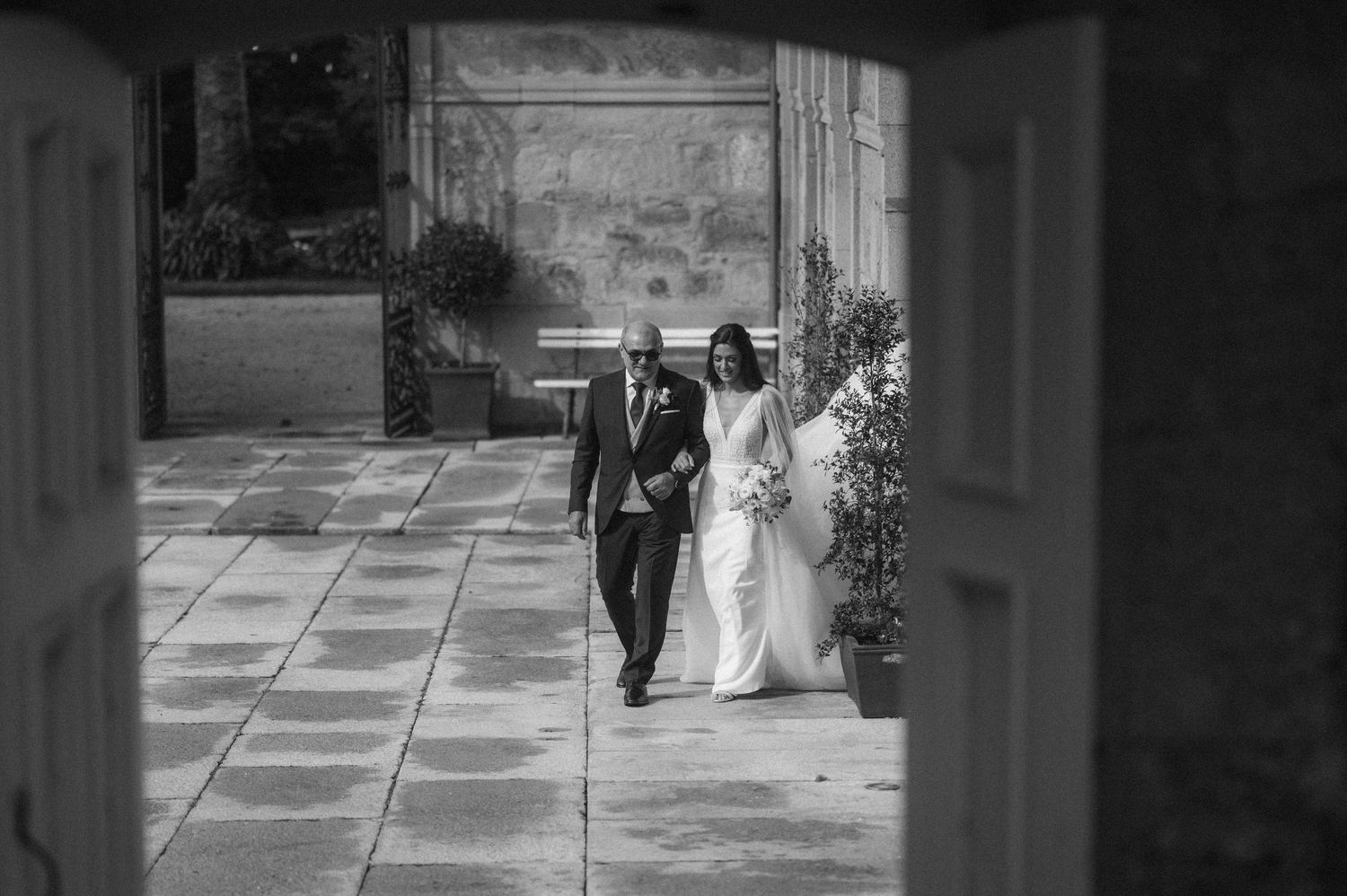 Black and white photo of a bride and groom walking down a stone pathway at their outdoor wedding ceremony.