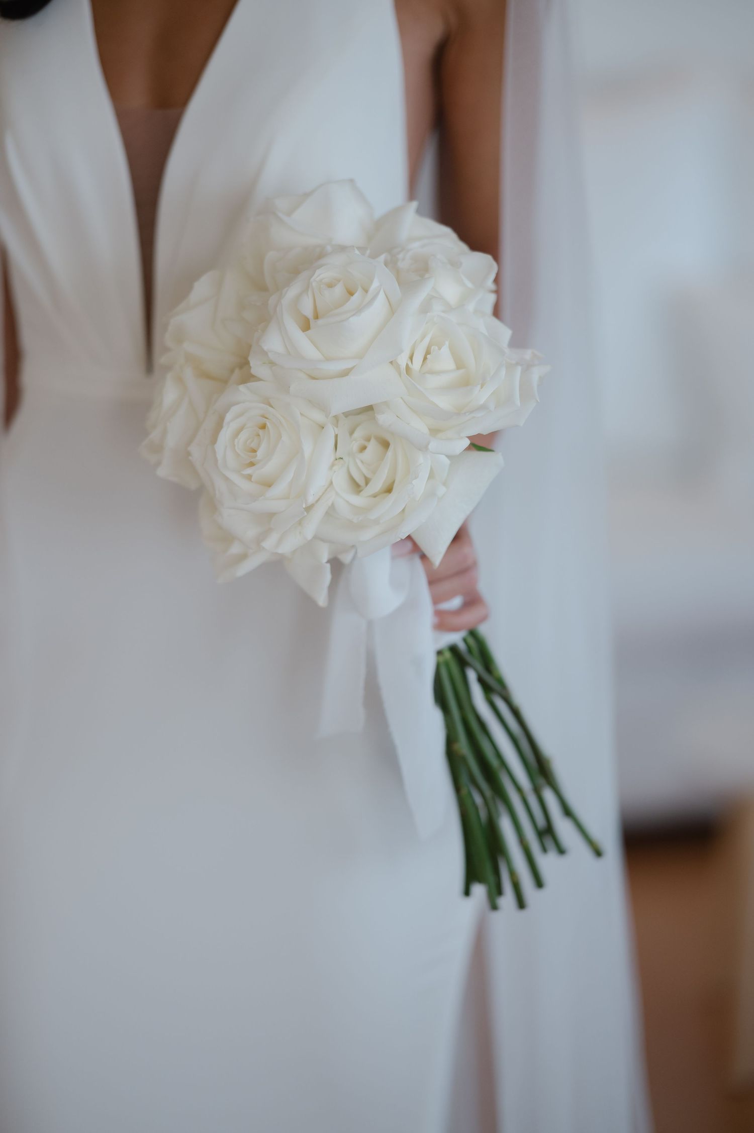 Elegant white rose wedding bouquet held against a light background.