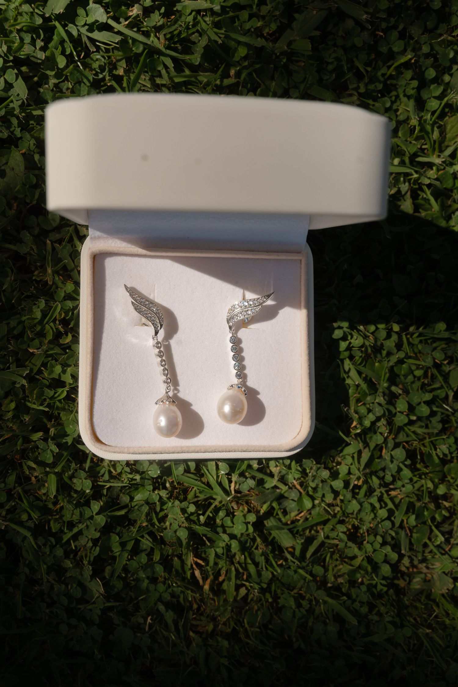 Delicate silver saxophone-shaped earrings with pearl accents displayed in white jewelry boxes on grass.