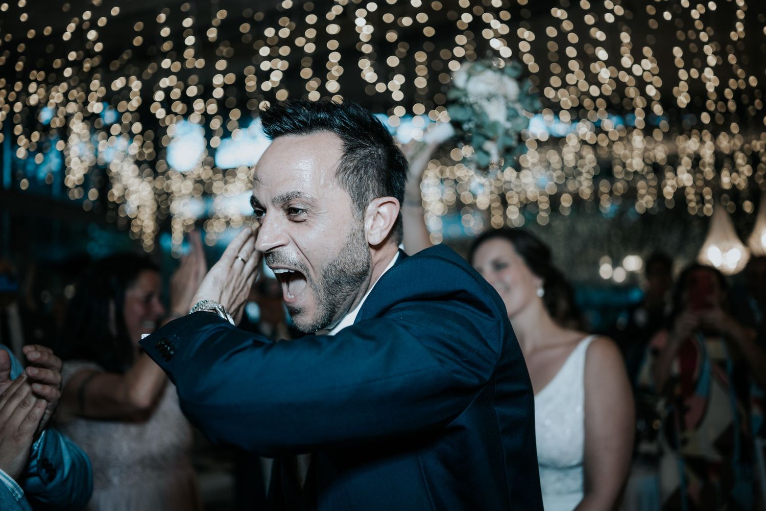 A couple sits together at a reception with glittering bokeh lights in the background.