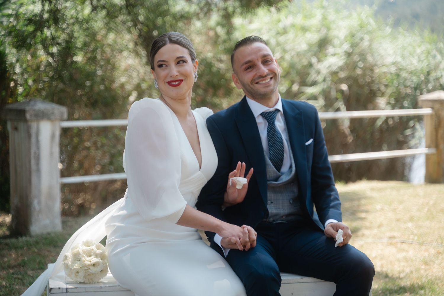 A joyful wedding couple shares a candid moment outdoors in a sunny garden setting.