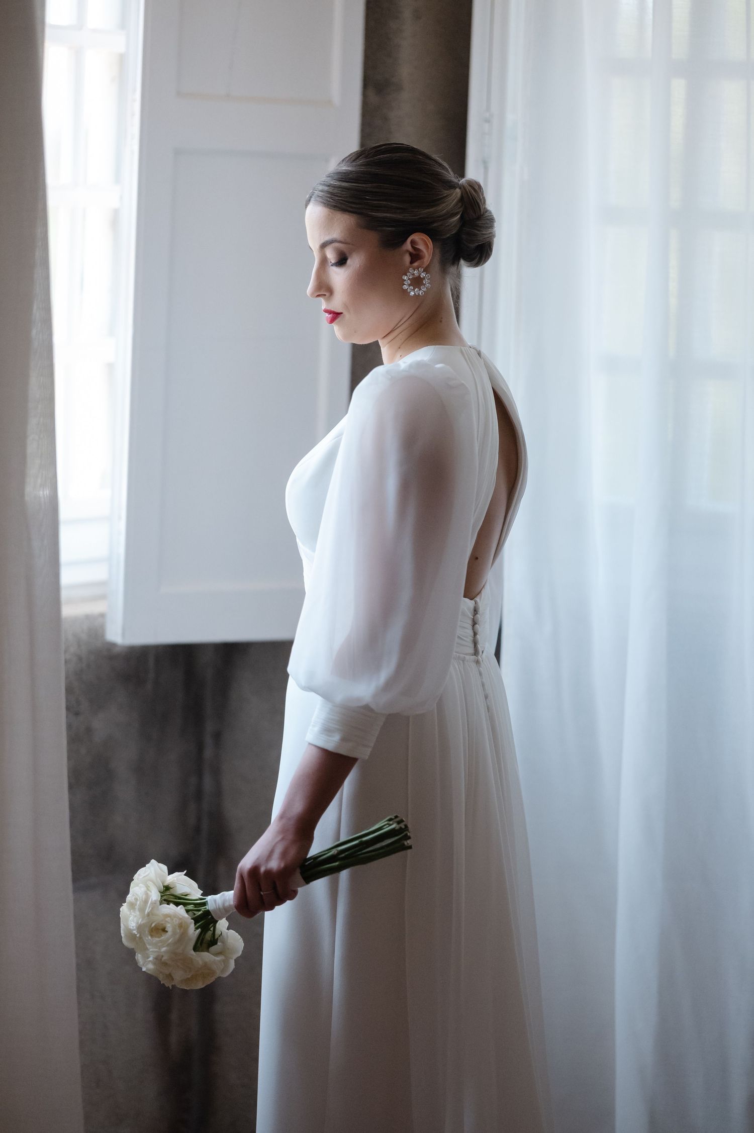 Elegant white wedding dress with long sleeves and flowing skirt captured in soft window light.