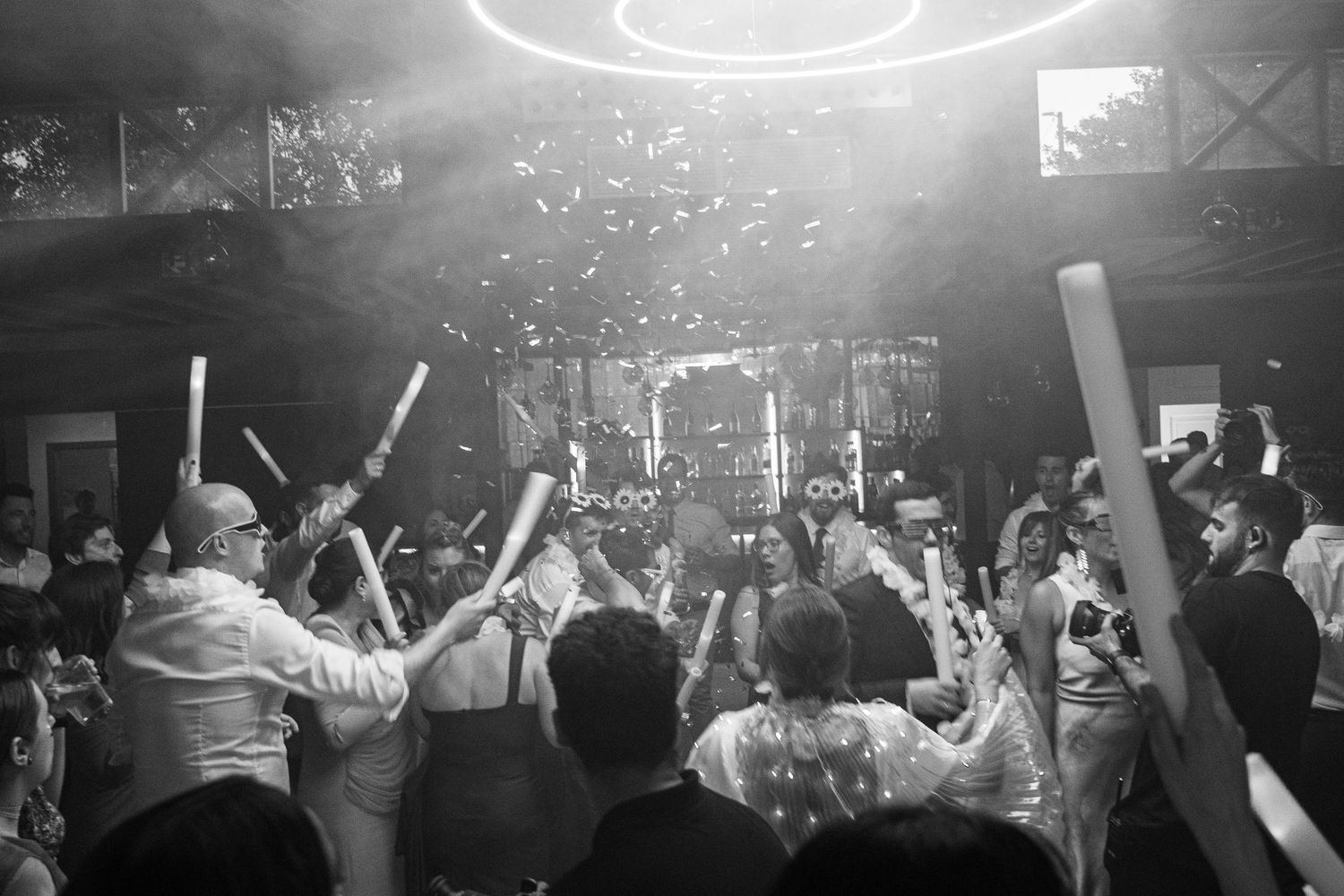 Party crowd dancing with raised arms under bright spotlights in a dark nightclub atmosphere.