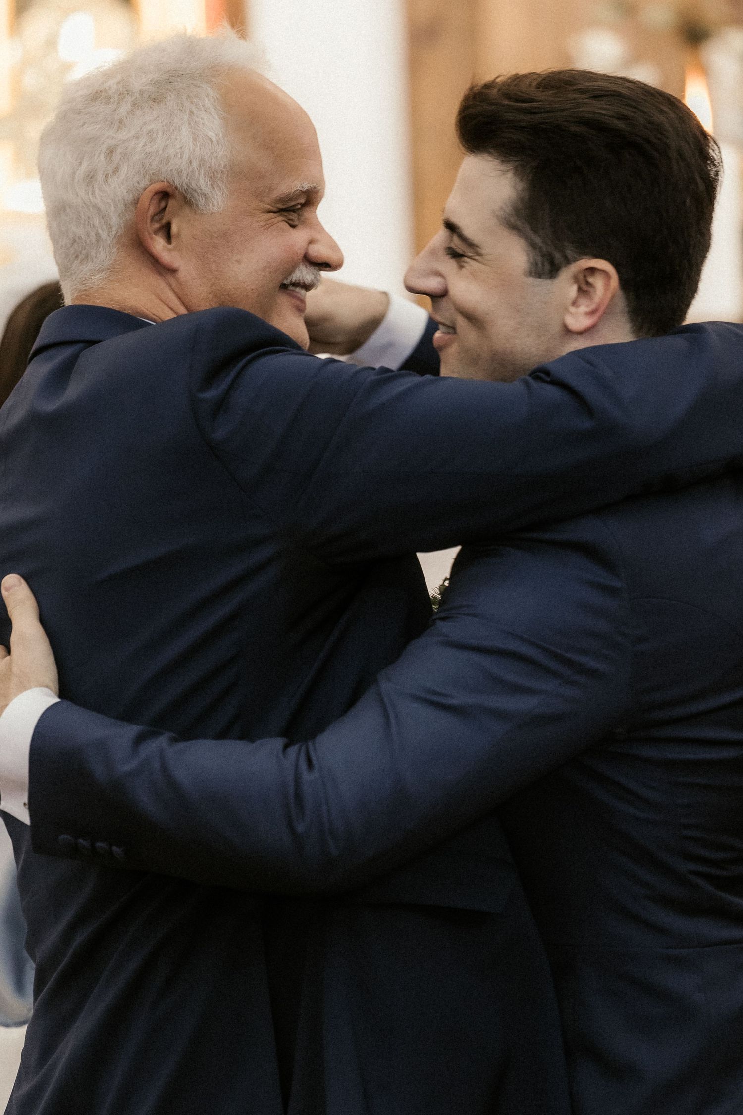 Two figures in dark suits embrace in a side-by-side sequence of candid photos showing warmth and camaraderie.