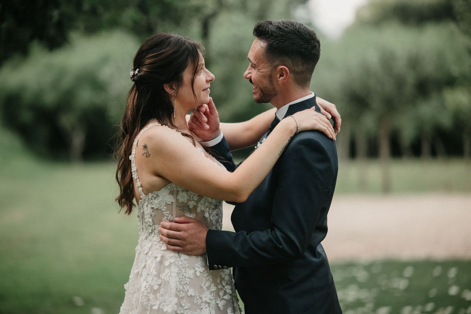 A romantic couple in wedding attire embrace outdoors in a lush green garden setting during their special day.