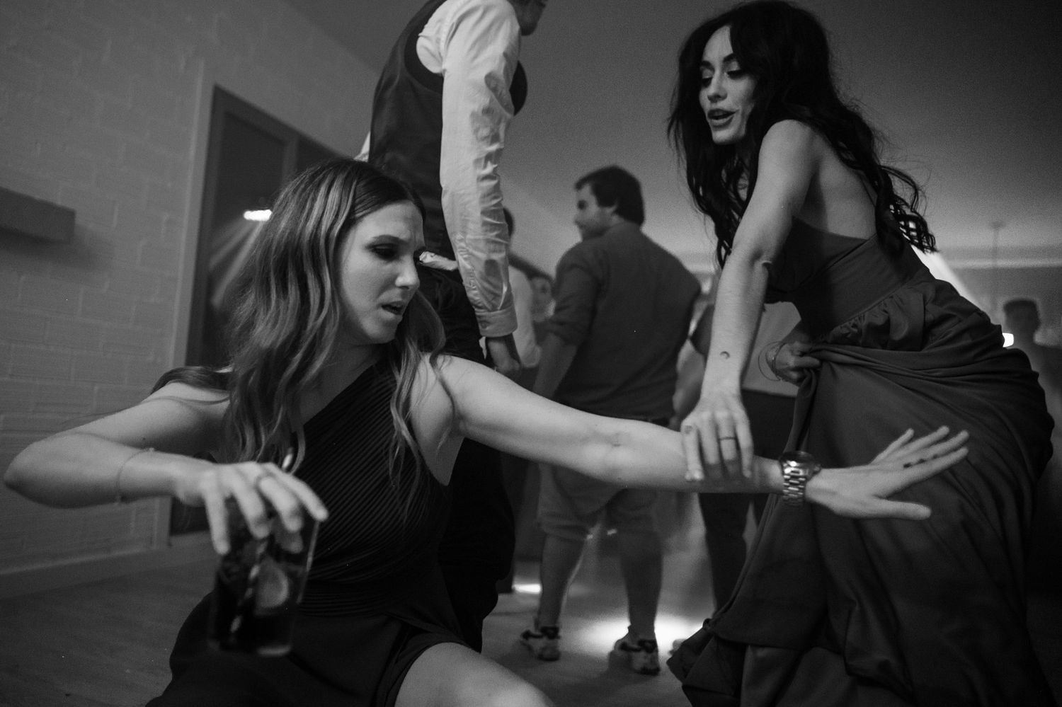 Black and white shot of people dancing and enjoying themselves at a social gathering with dramatic lighting.