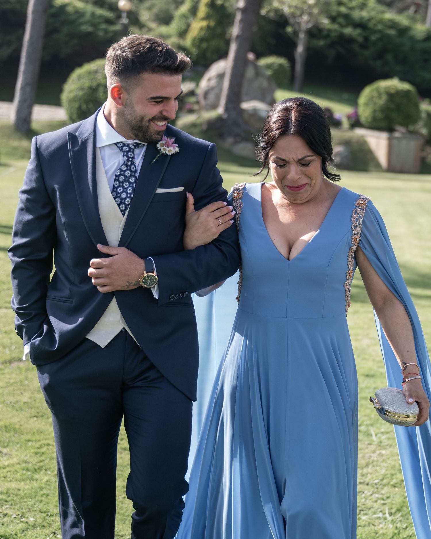 A couple in formal attire share a joyful moment together outdoors, with the woman wearing a light blue dress.