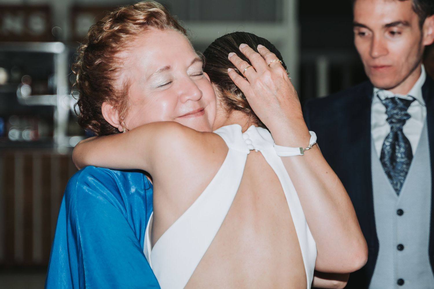 Two people share an emotional embrace at a formal event, with one wearing a bright blue outfit and one in white.
