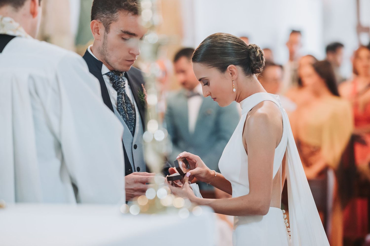 A couple exchanges rings during an elegant wedding ceremony as guests look on in the background.