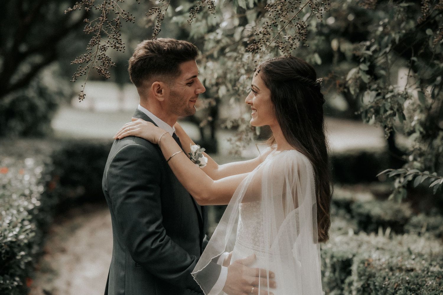 A romantic wedding couple embraces in a lush garden setting with soft natural lighting and ethereal atmosphere.