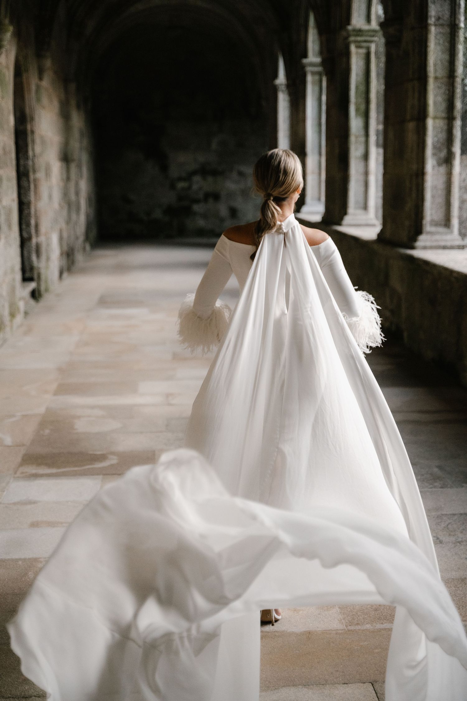 A flowing white wedding dress billows dramatically through a stone archway corridor.