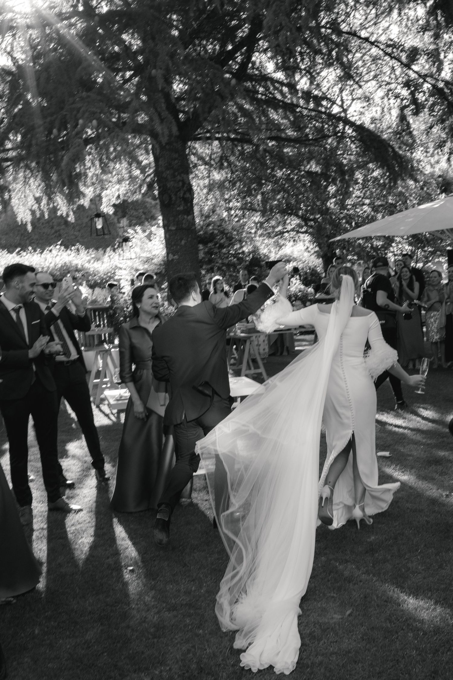A black and white photo series captures a bride and groom dancing joyfully at an outdoor garden wedding reception.