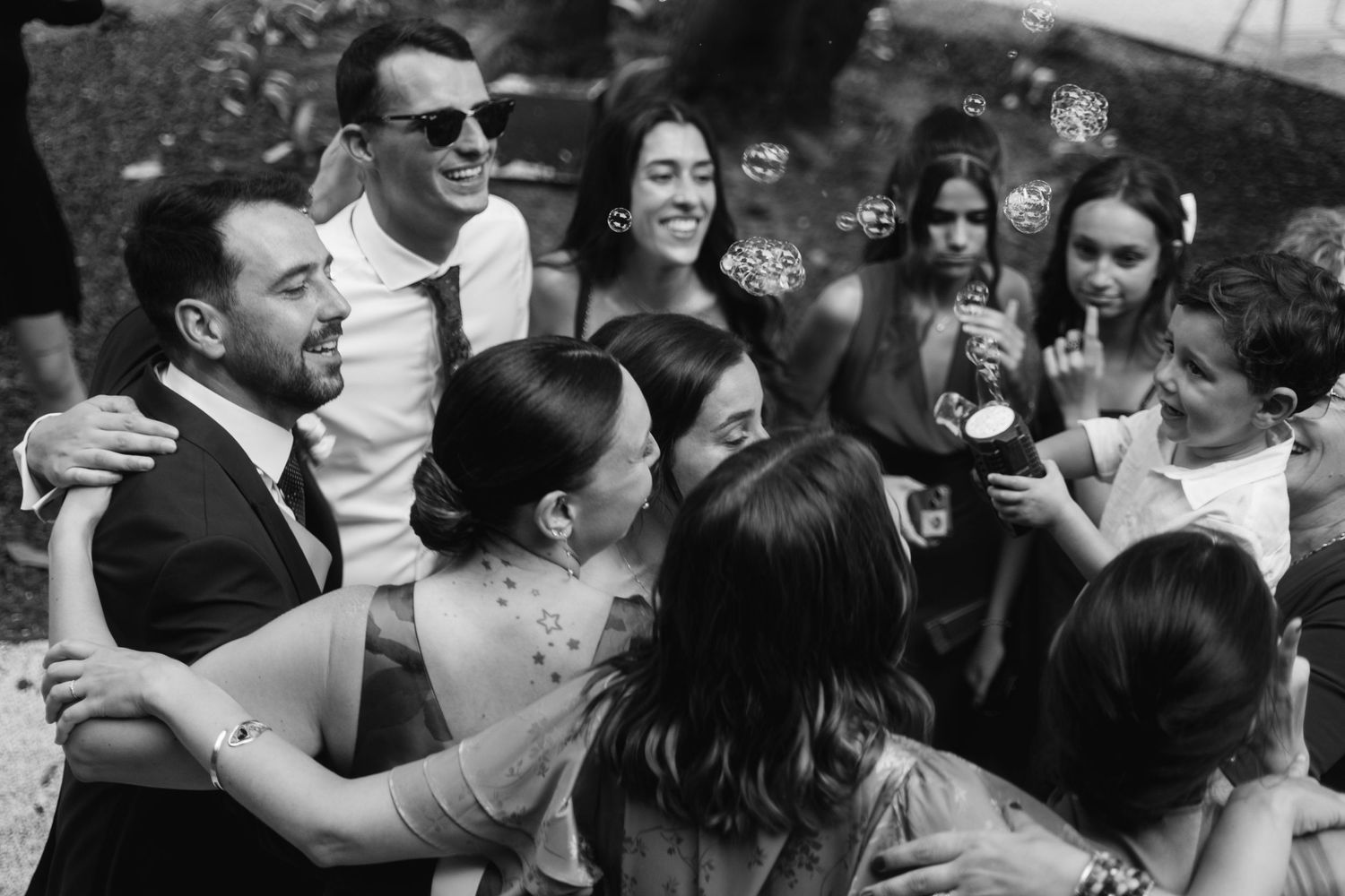 Wedding guests share joyful embraces and celebratory hugs during an outdoor reception gathering.