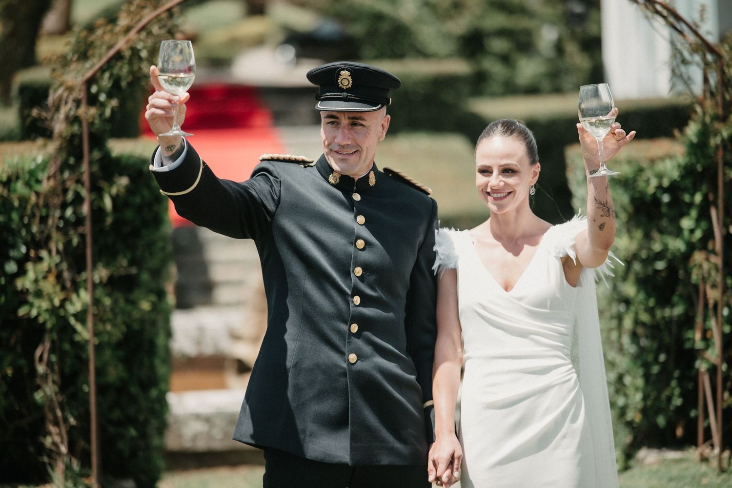 Wedding couple walking outdoors in formal attire with traditional military dress uniform.