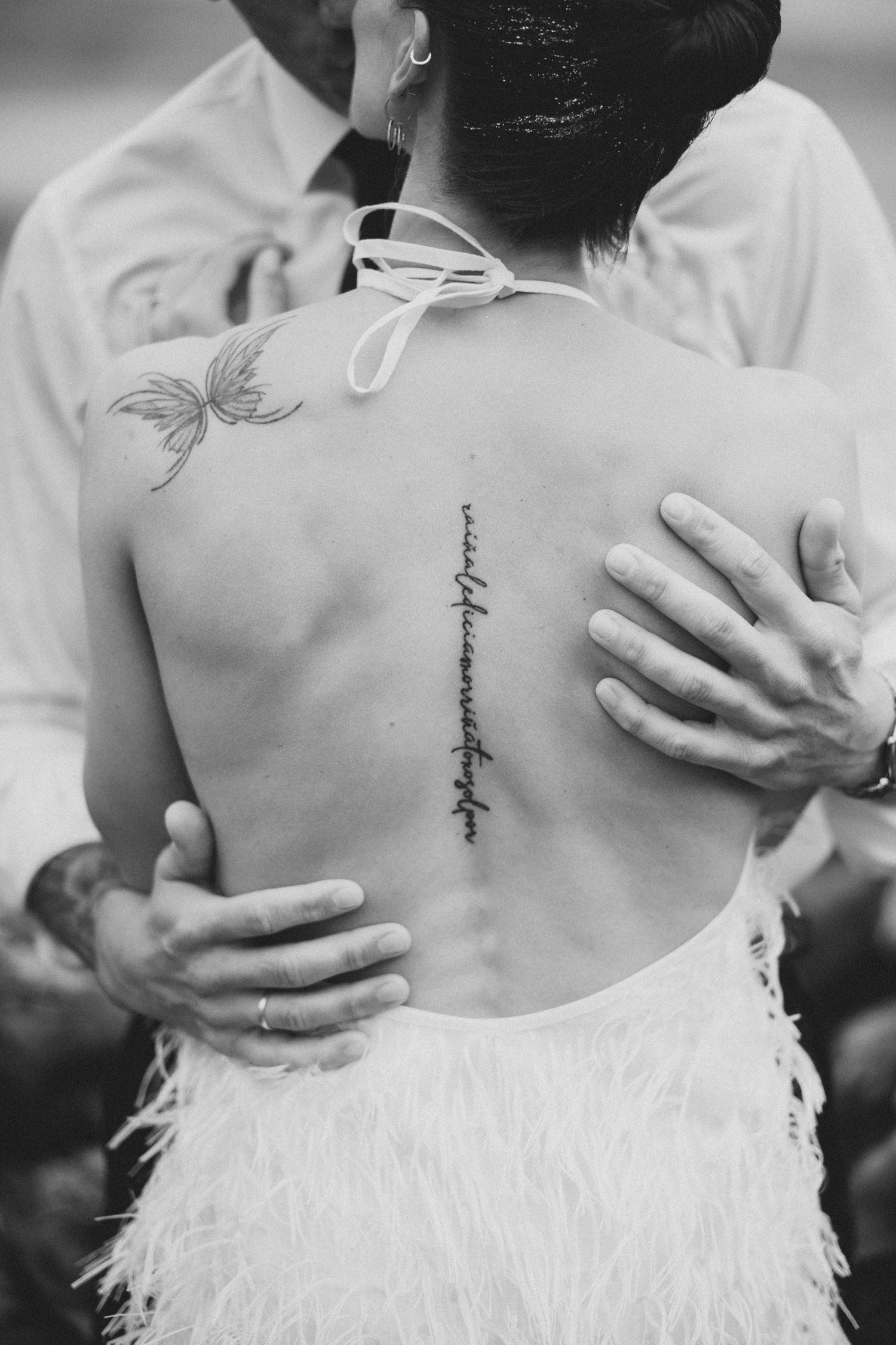 A close-up view of a delicate spine tattoo on someone wearing a white feathered dress.