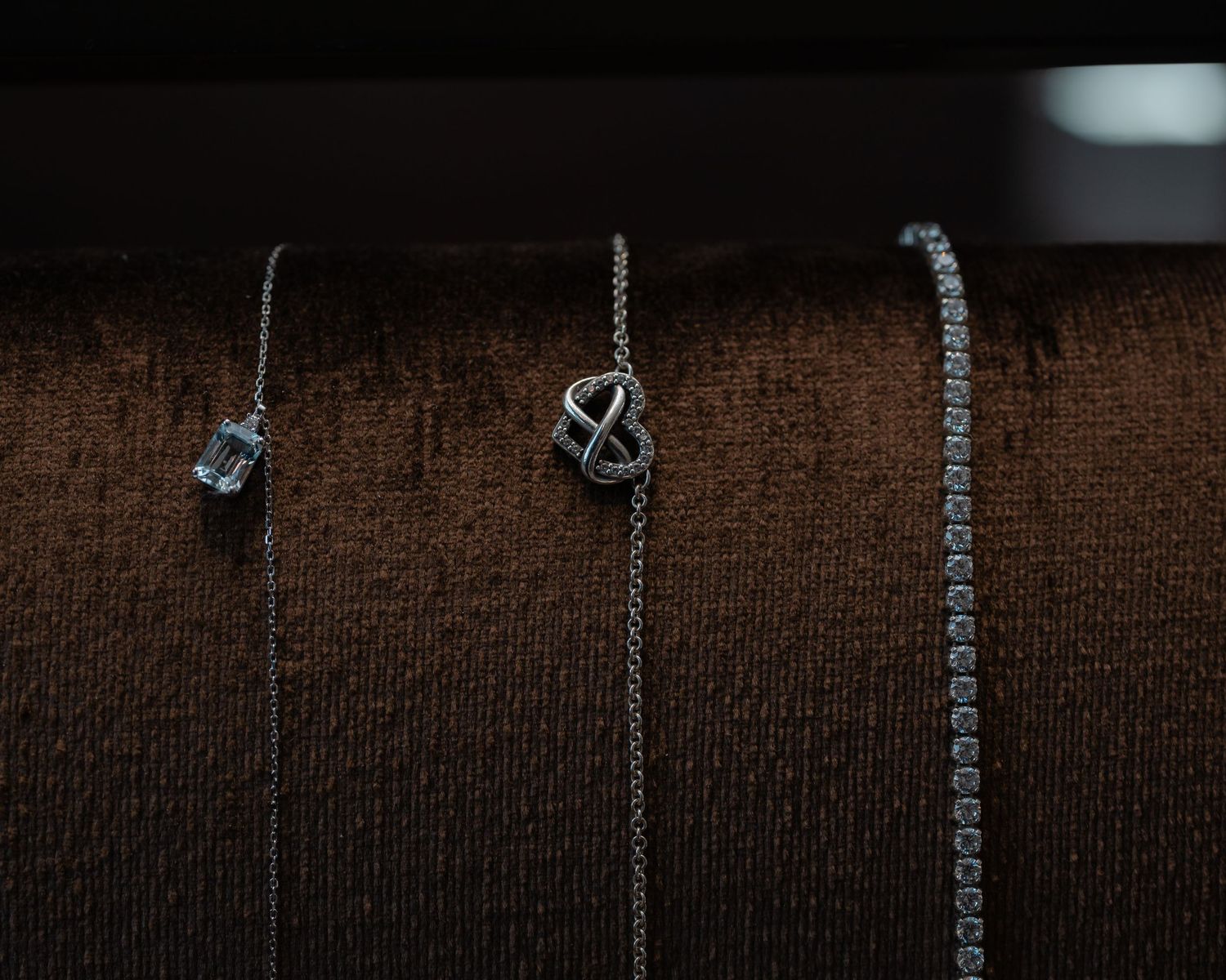 Delicate necklaces hanging against a textured brown fabric background.