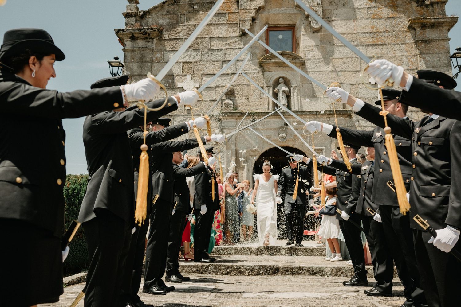 Wedding party celebrating outside a stone church with bubbles and festive atmosphere.