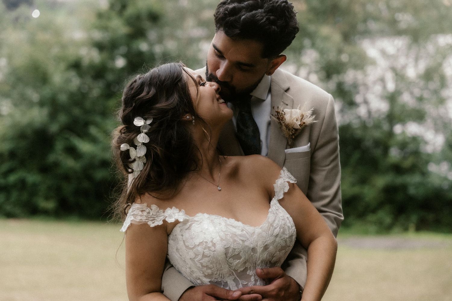 A couple in wedding attire embraces tenderly in a lush outdoor garden setting.