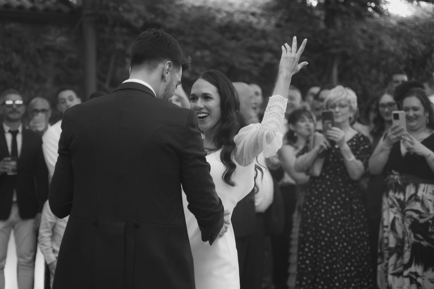 Black and white photo showing joyful guests celebrating at an outdoor wedding reception.