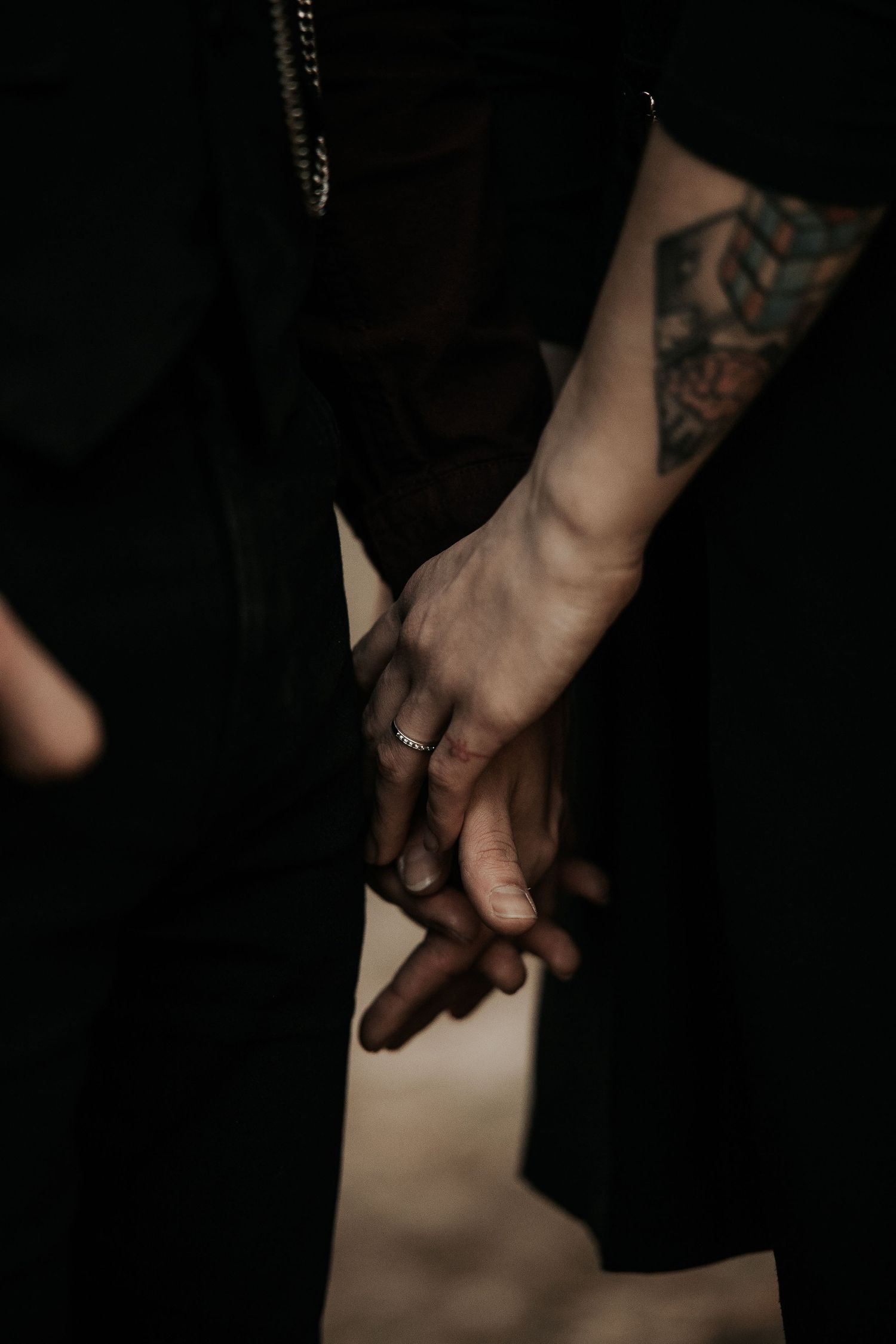 Close-up shots of hands with tattoos against a dark background show intimate gestures.