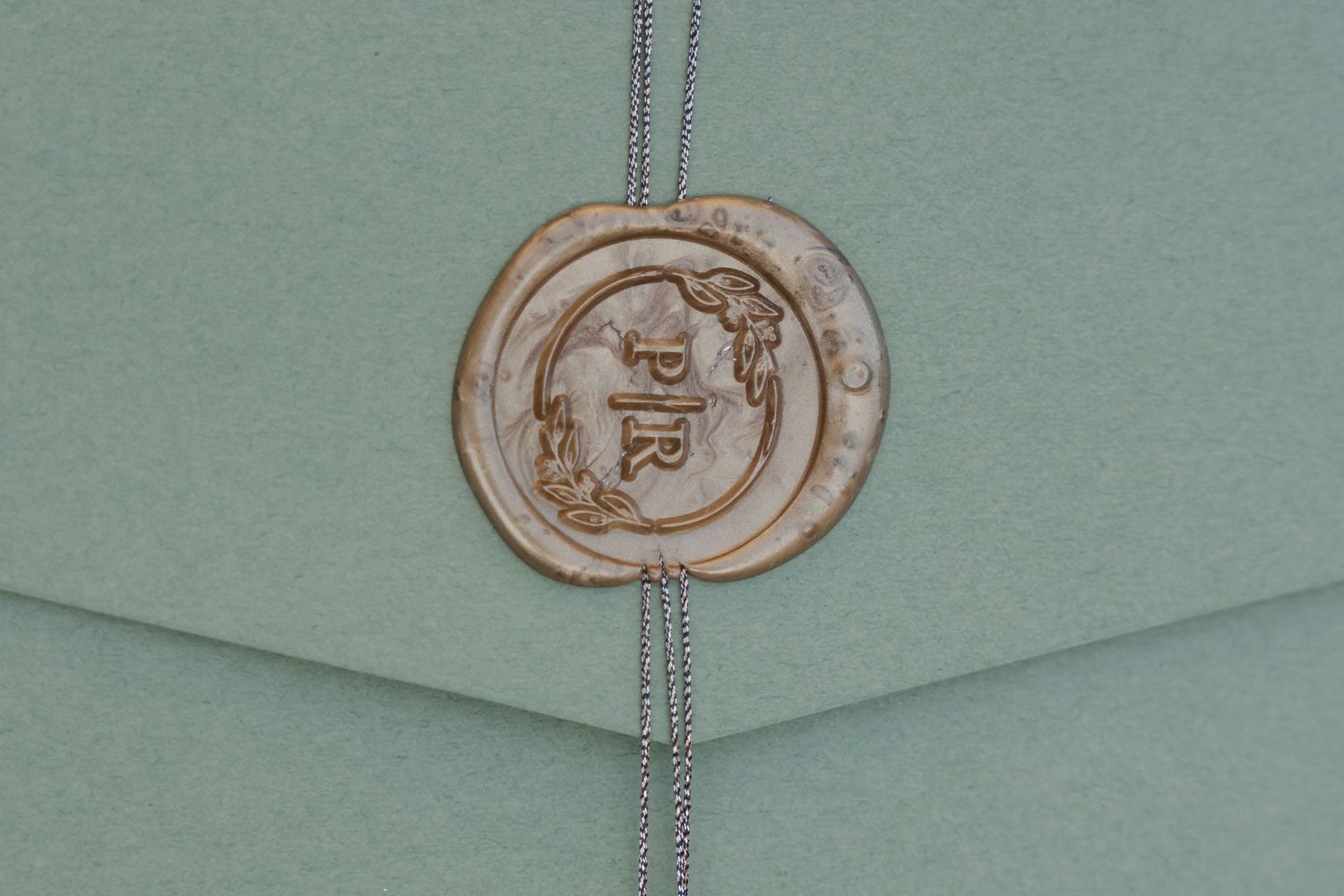 A close-up view of a wax seal with a decorative emblem on a light teal colored paper background.