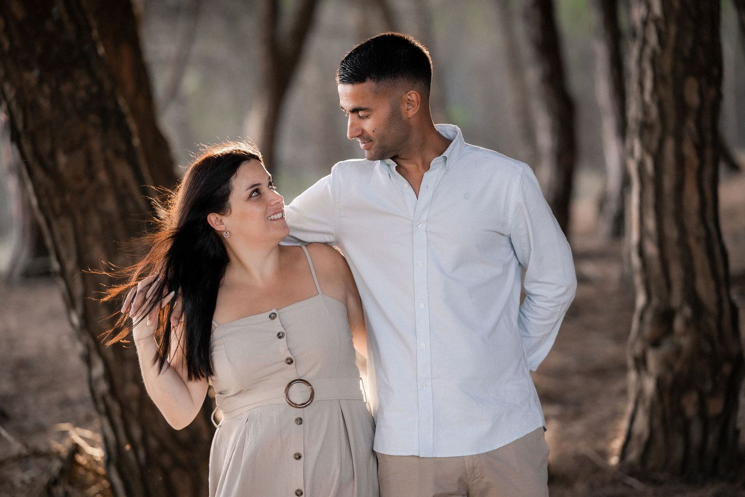 Romantic couple in white outfits embracing in a forest setting during golden hour.