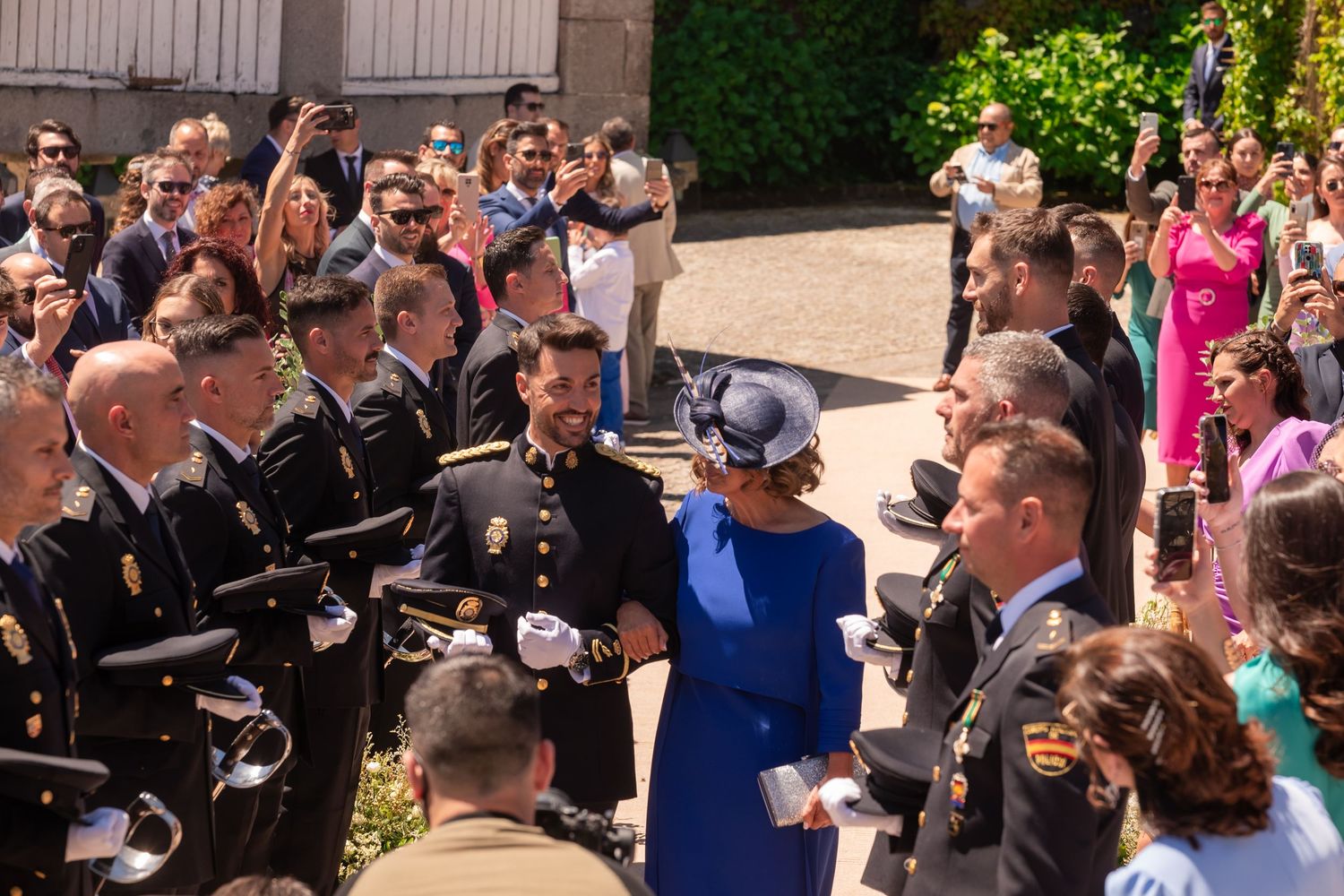 A crowd of people in formal attire gather outdoors on a sunny day during a special event.