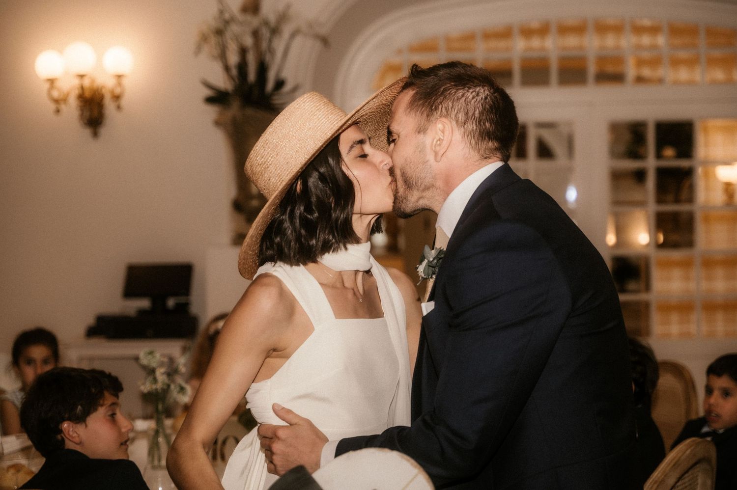 A couple shares a romantic kiss during their wedding reception in an elegant ballroom with warm lighting.