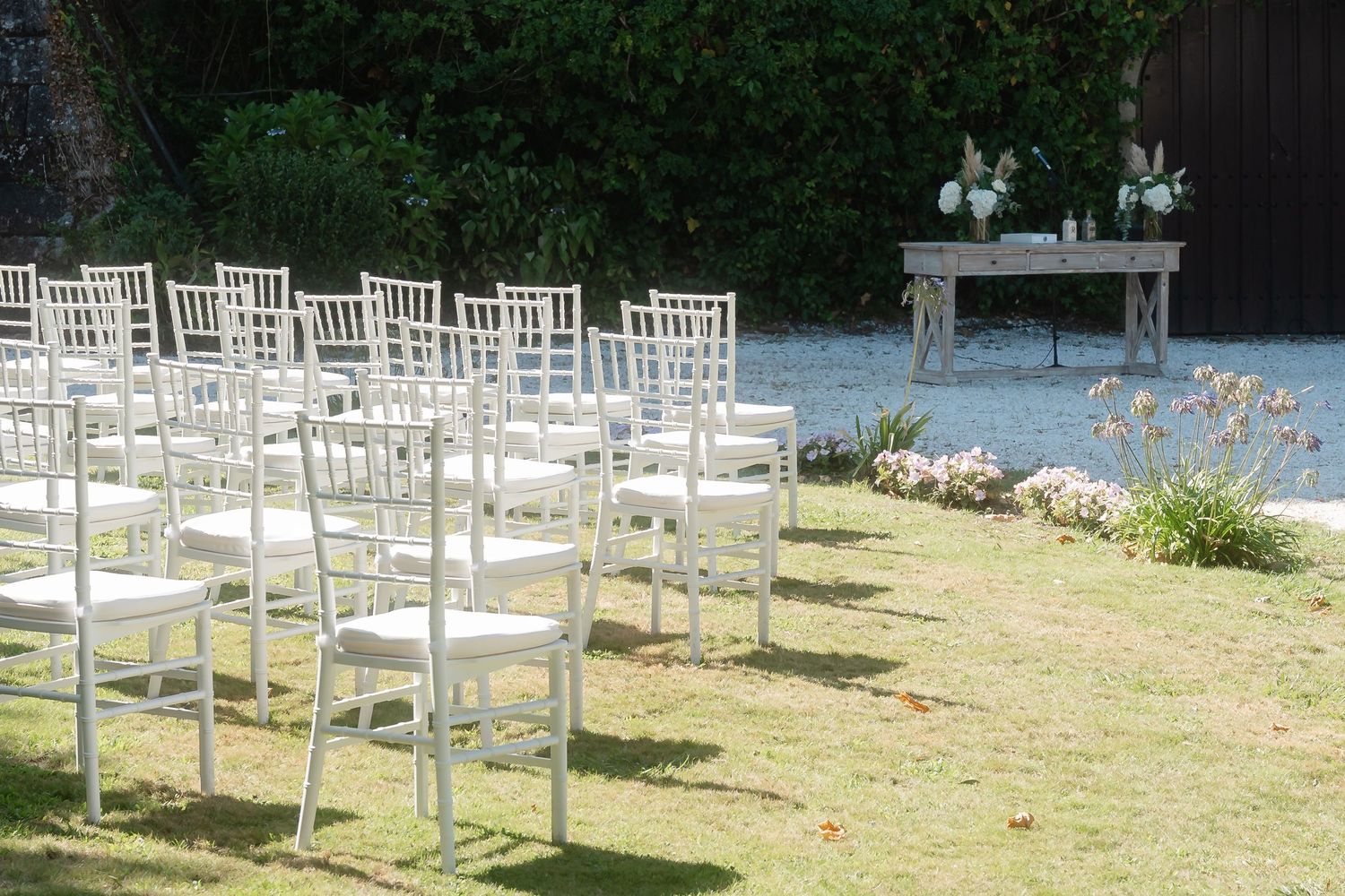 White wooden chairs arranged in rows for an outdoor wedding ceremony on a sunny lawn.