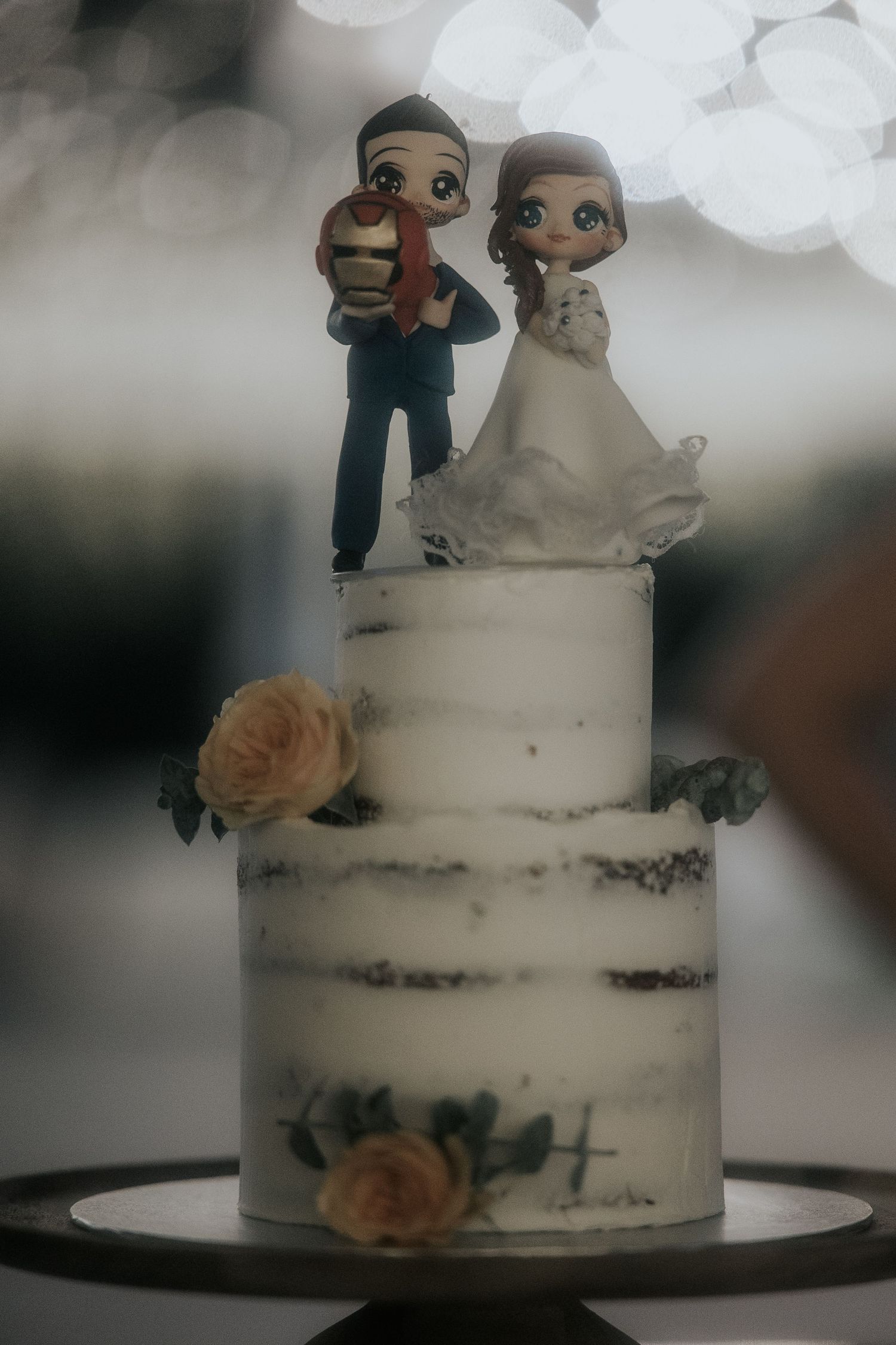 White semi-naked wedding cake decorated with peach roses and custom bride and groom cake toppers.