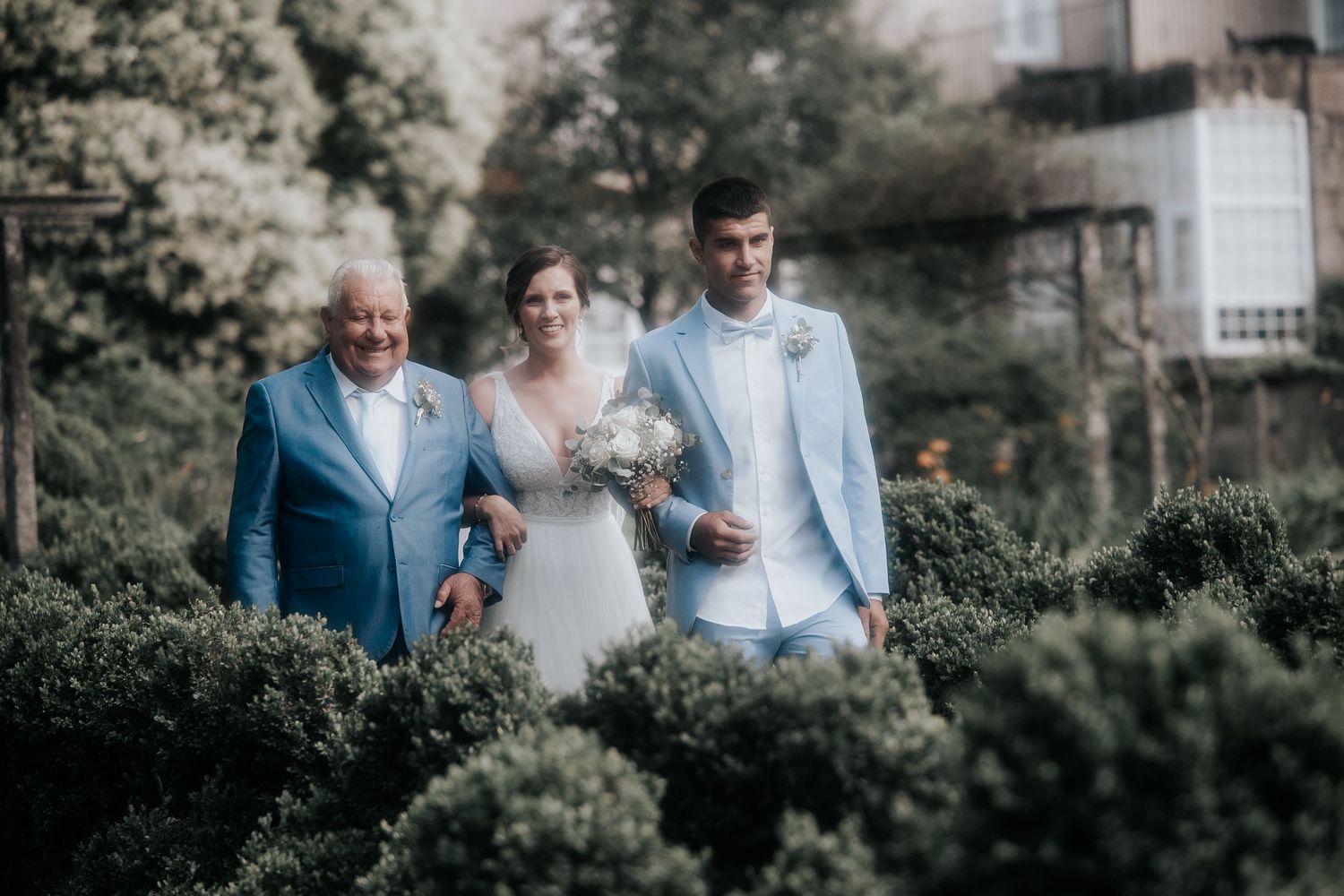 Wedding party gathers outdoors in an elegant garden setting with natural greenery and soft lighting.