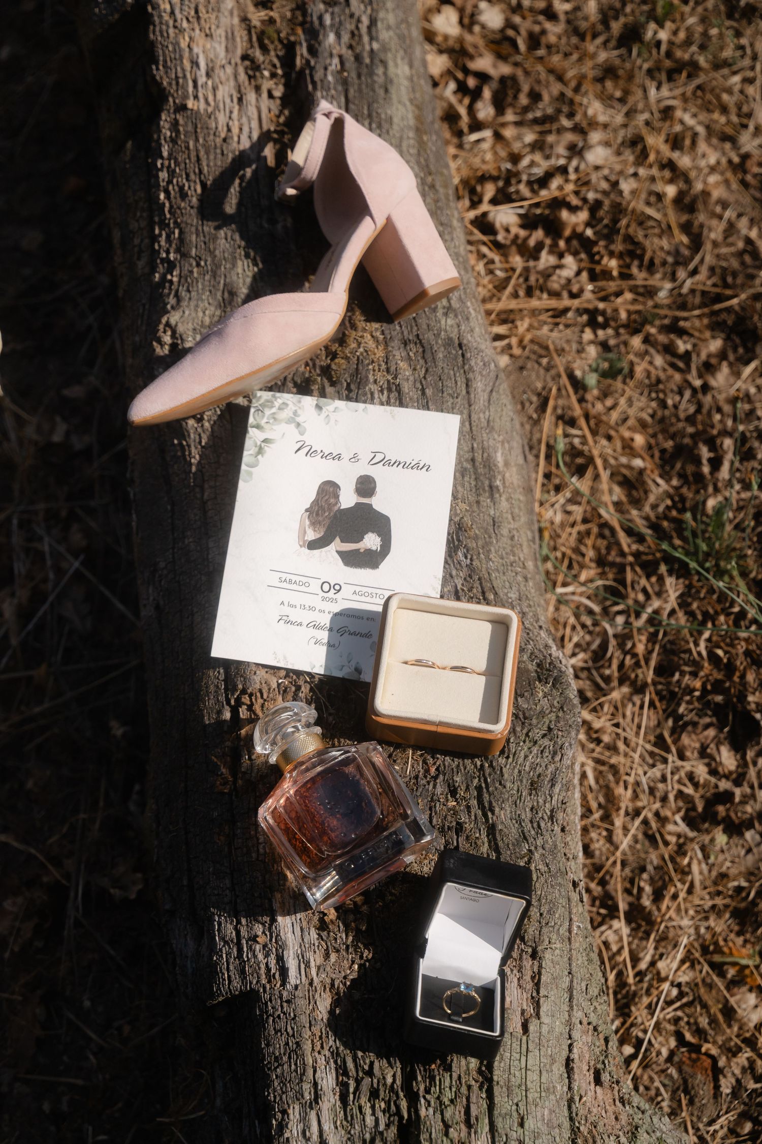 Wedding accessories including invitation, perfume, and jewelry arranged artistically on a rustic wooden surface.