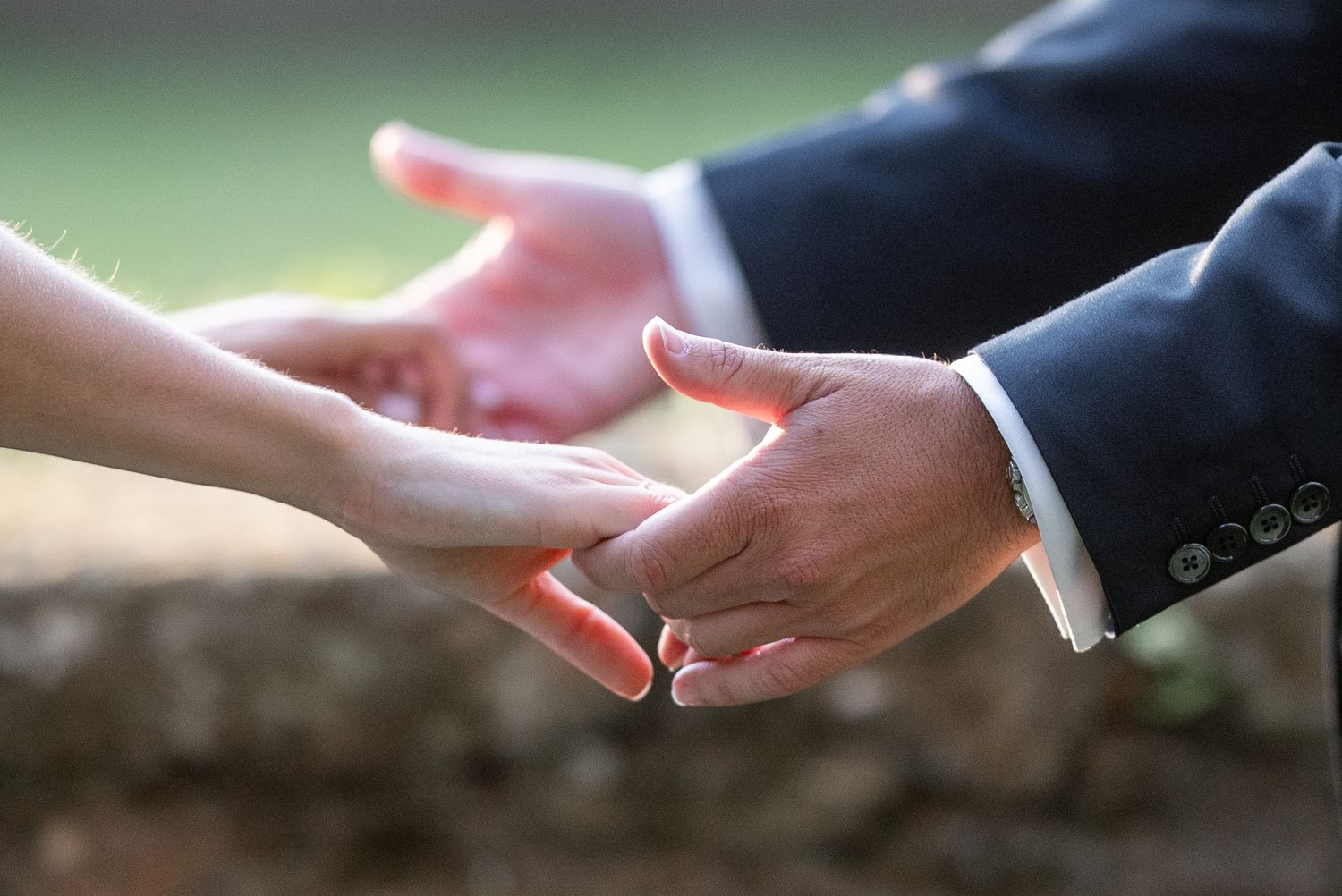 Close up of hands exchanging wedding rings during a marriage ceremony against a blurred background.