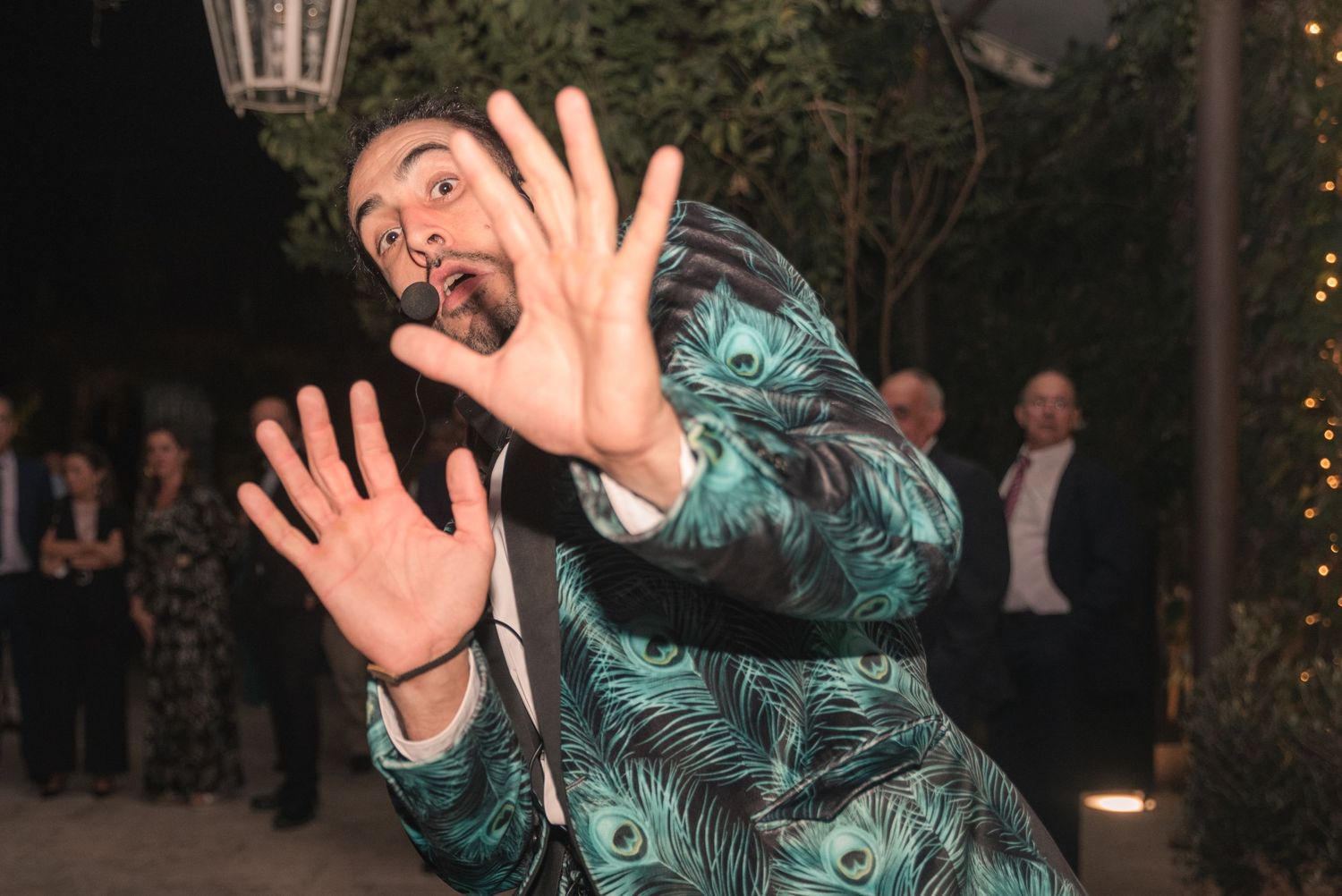 A person in a green tropical print suit jacket makes an exaggerated expression while posing at a nighttime event.