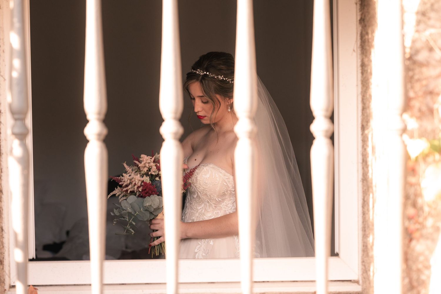A bride in a white gown stands behind white pillars in an elegant venue with warm lighting.