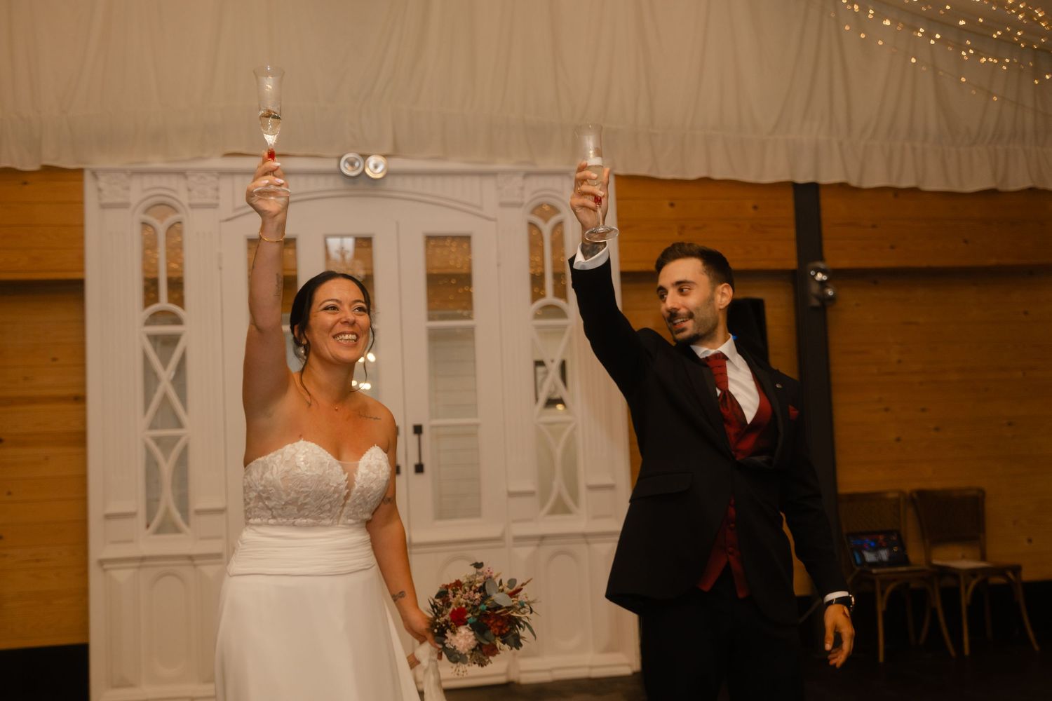 Wedding couple and guests dance together on a wooden floor during a joyful reception celebration.