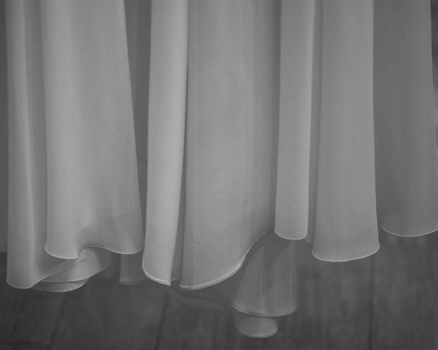 Close-up view of white curtain panels with soft folds creating a minimalist vertical pattern in grayscale.